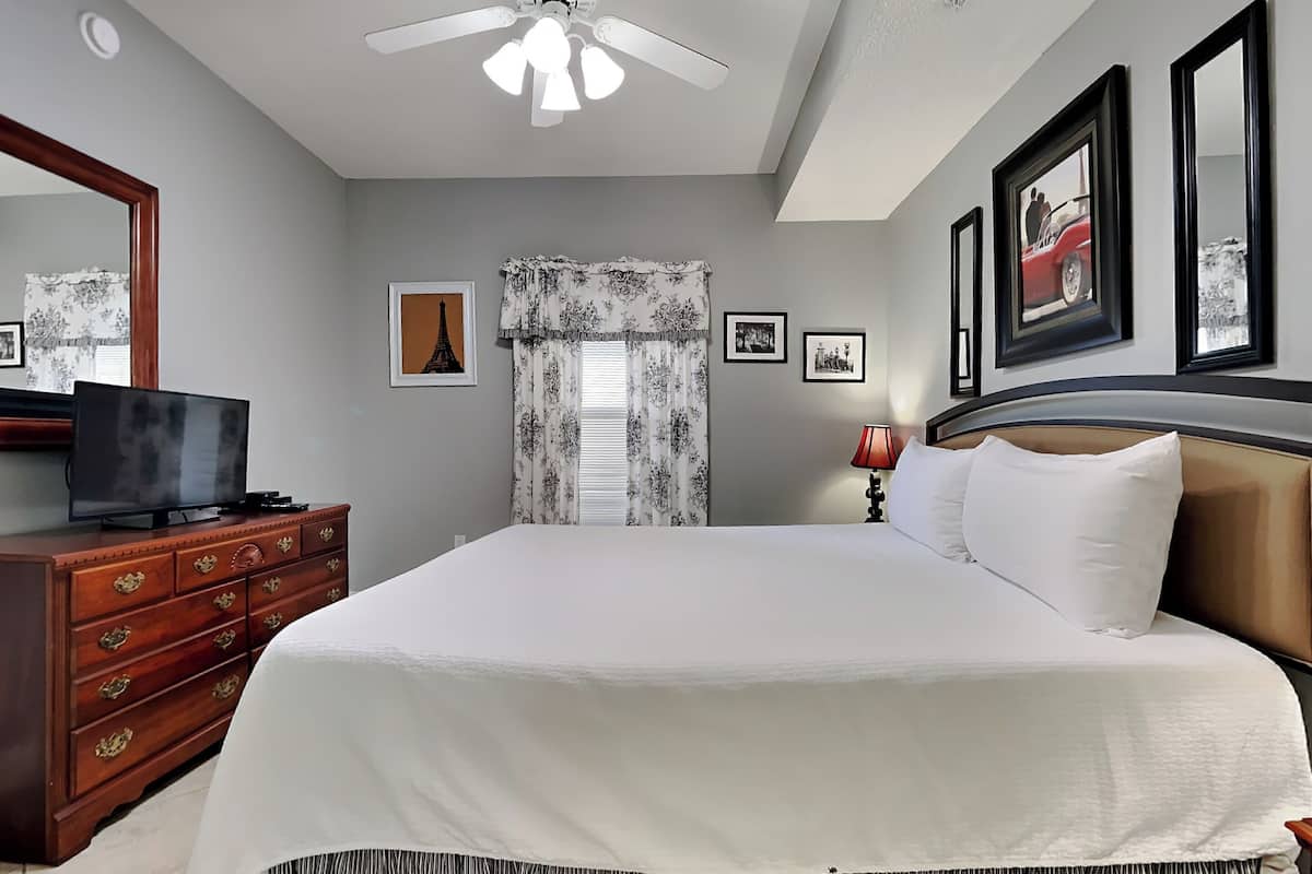 A hotel room with a large bed, a ceiling fan, a television on a wooden dresser, and framed pictures on the wall.