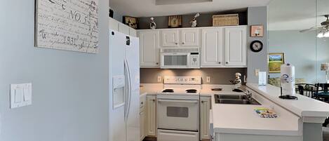 A compact kitchen with white cabinets, a refrigerator, a microwave, an oven, and a sink.
