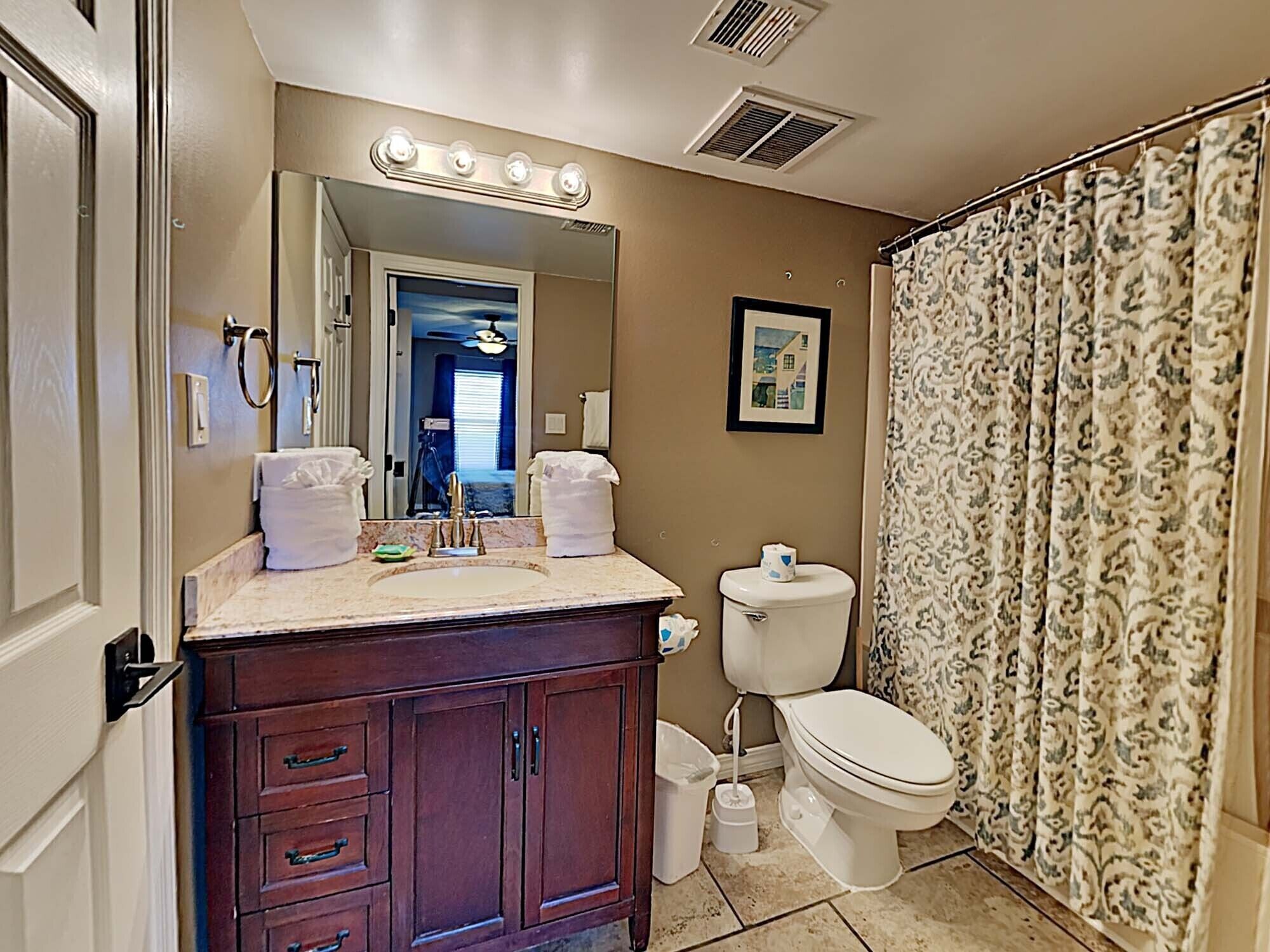 A bathroom with a vanity, sink, mirror with lights, toilet, and patterned shower curtain.