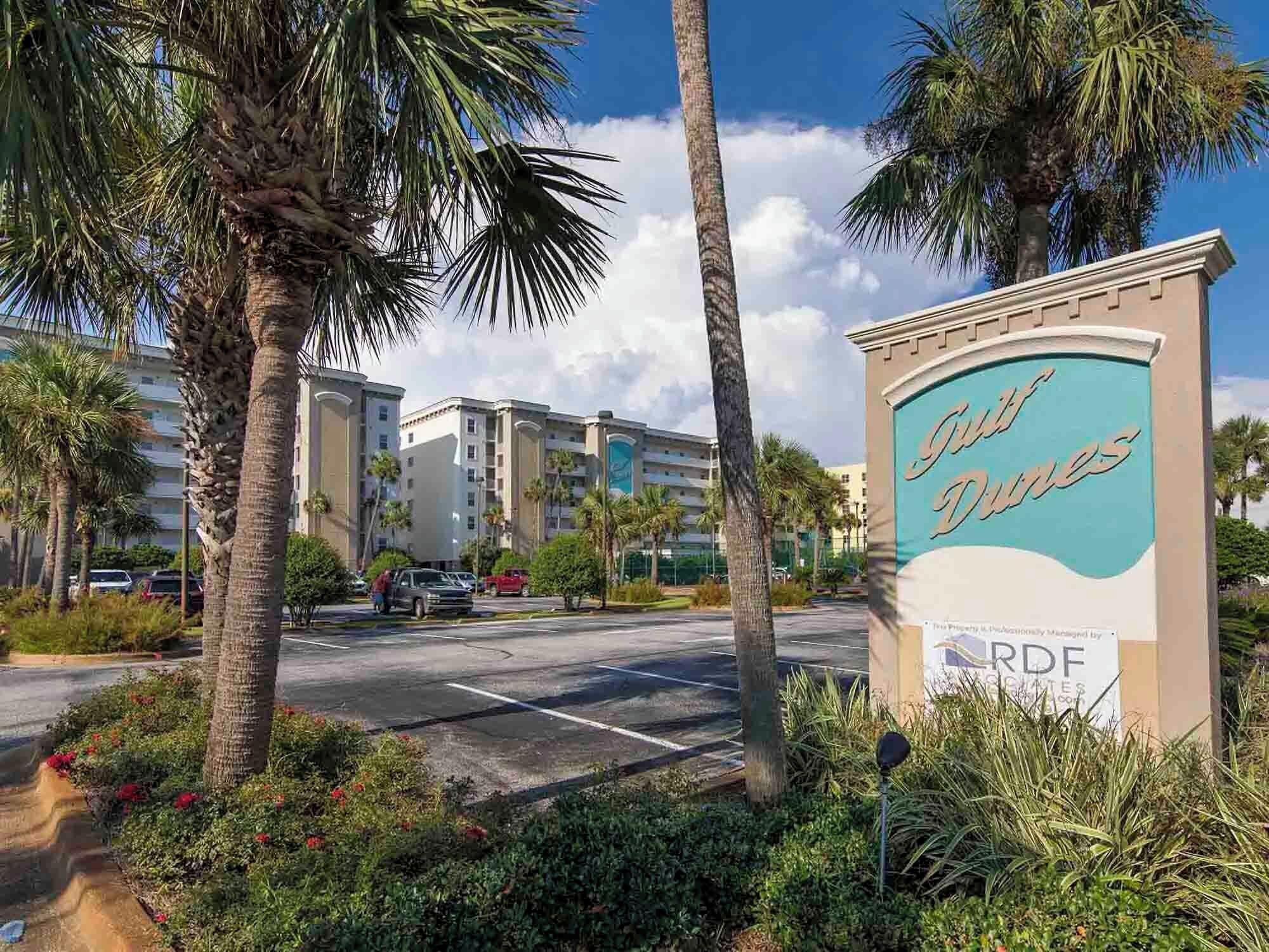 Entrada de un hotel con palmeras y un cartel que dice 'Duke Dunes'.