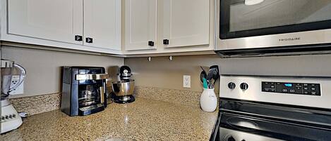 A kitchen with white cabinets, a stainless steel microwave, a coffee maker, and an oven.