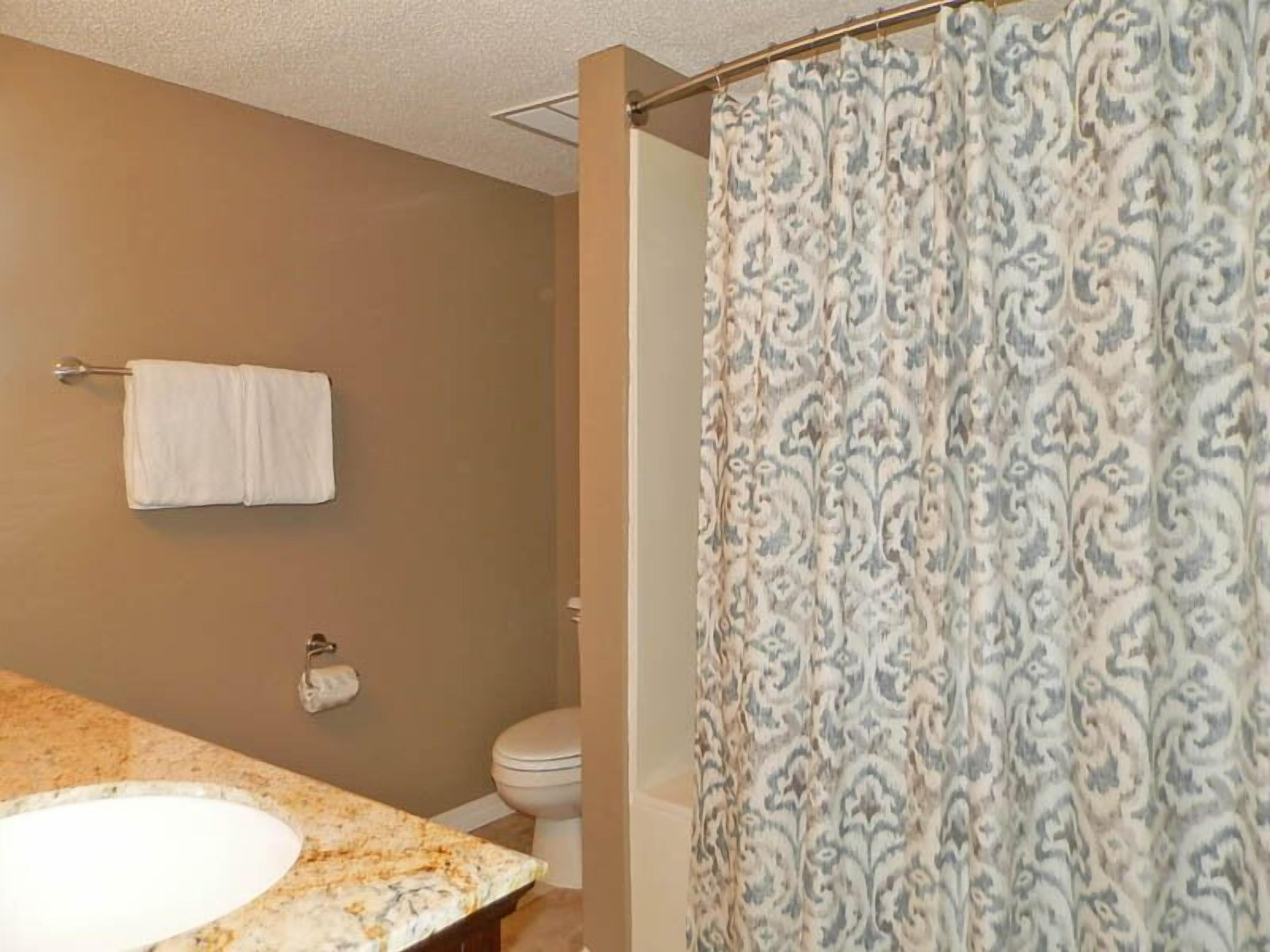A bathroom with a marble sink, a toilet, and a patterned shower curtain.