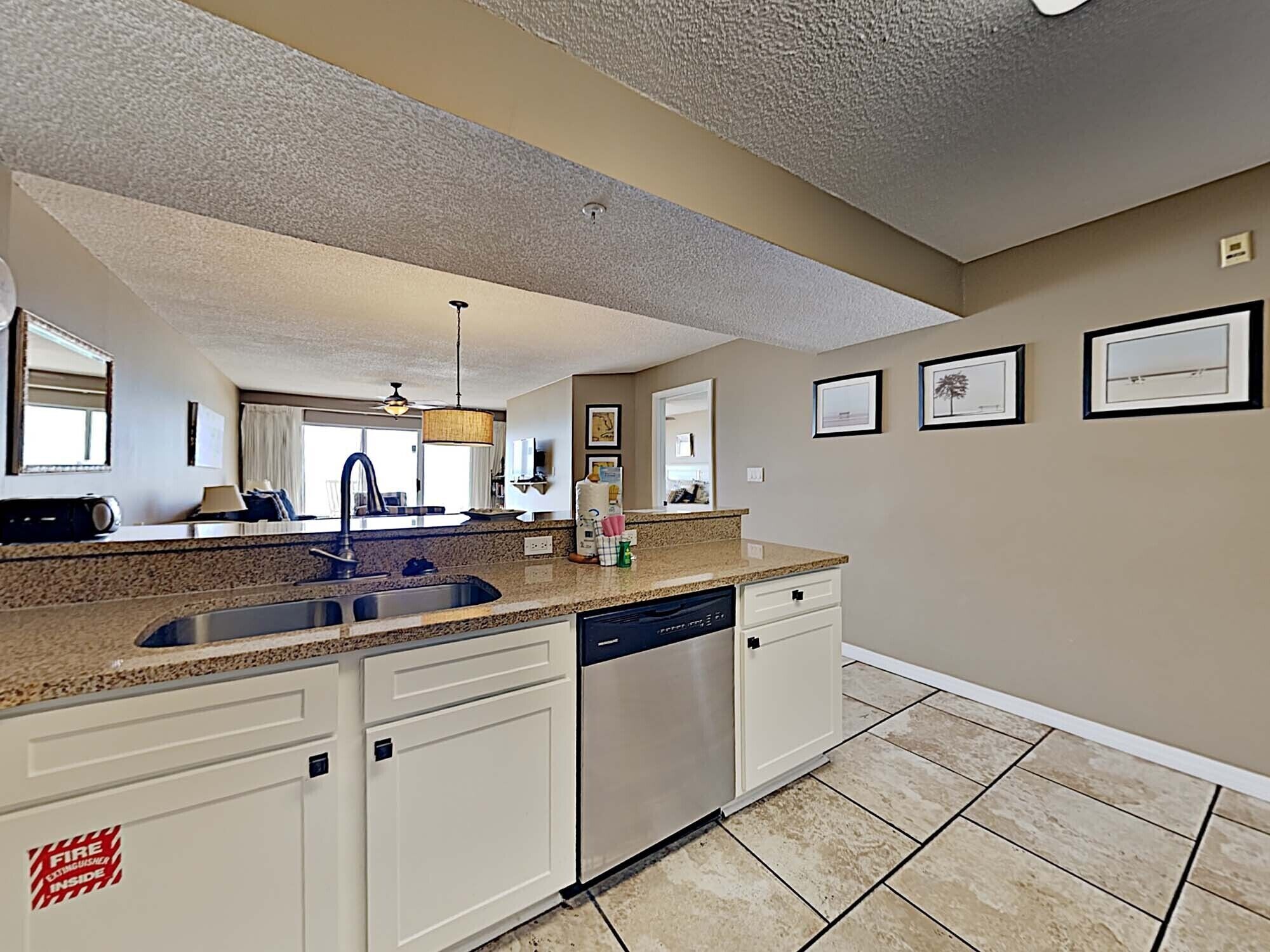 A kitchen with granite countertops, a dishwasher, and a sink. There are framed pictures on the wall.