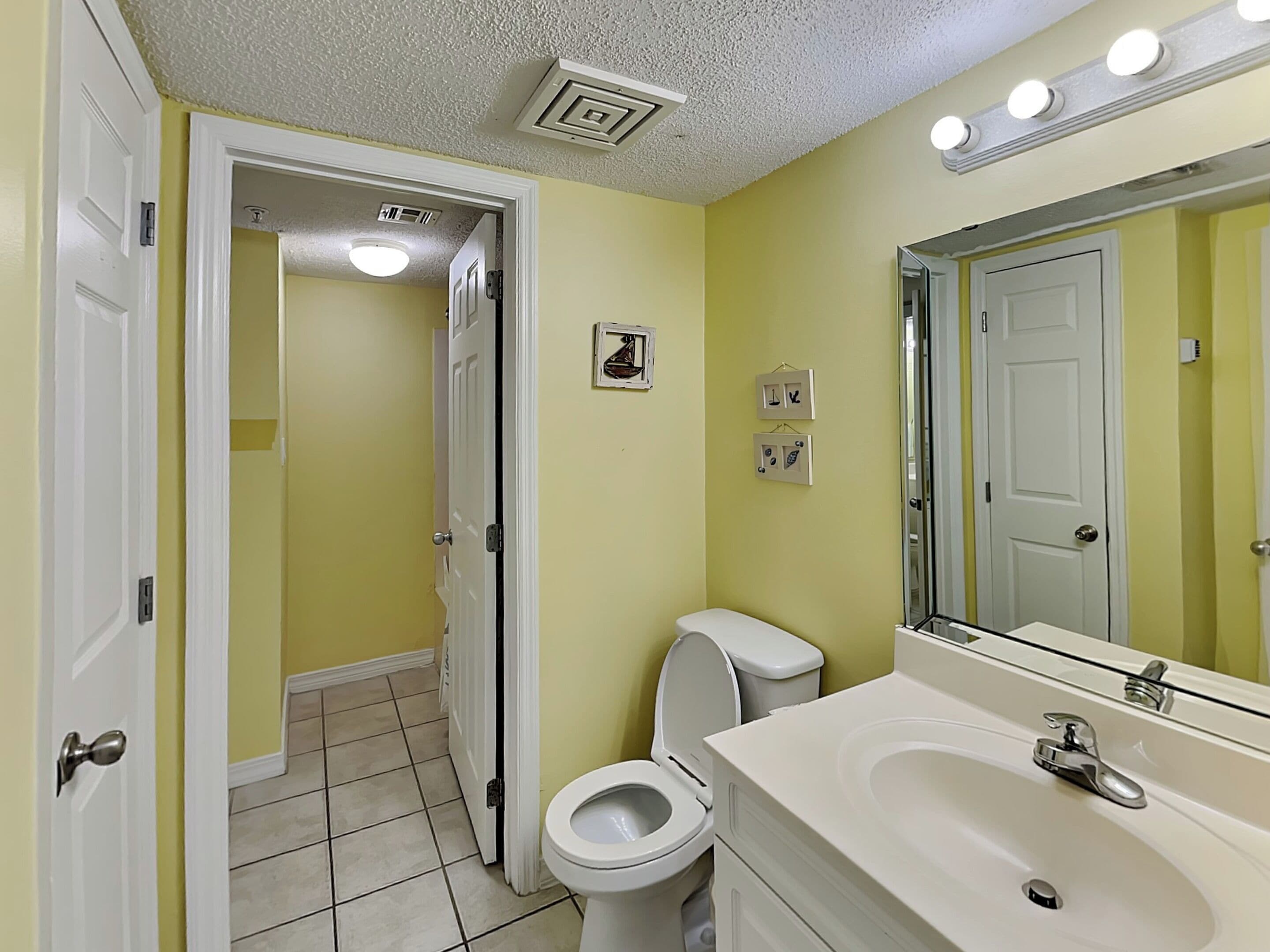 Un baño con inodoro, lavabo, espejo y una puerta que da a otra habitación.