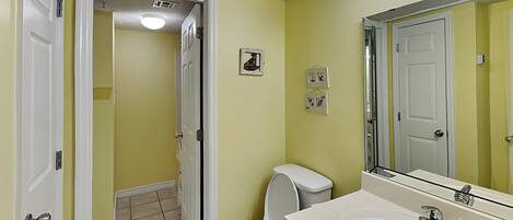 Un baño con inodoro, lavabo, espejo y una puerta que da a otra habitación.