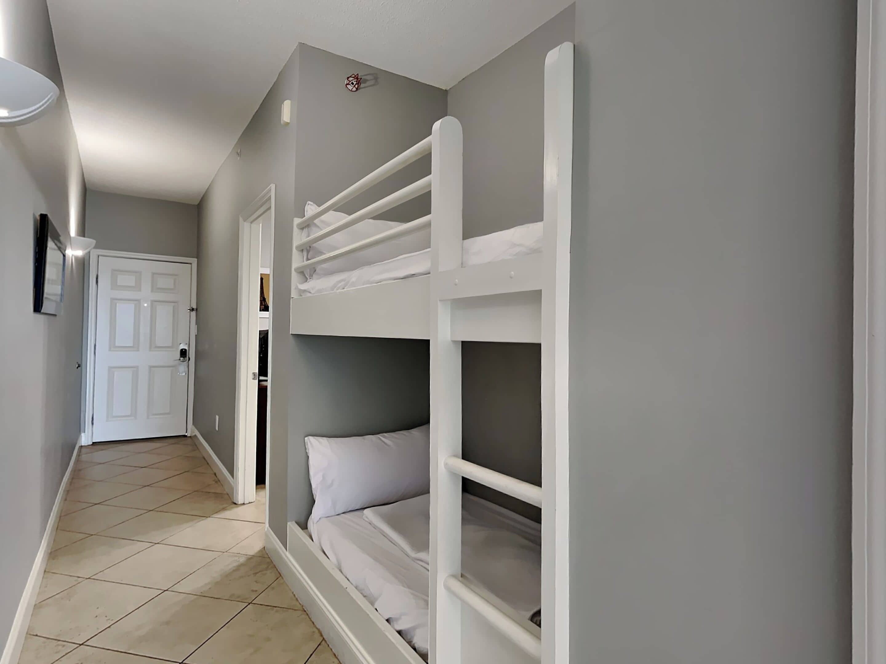 Um corredor com uma cama beliche, uma porta branca e um aparelho de iluminação.