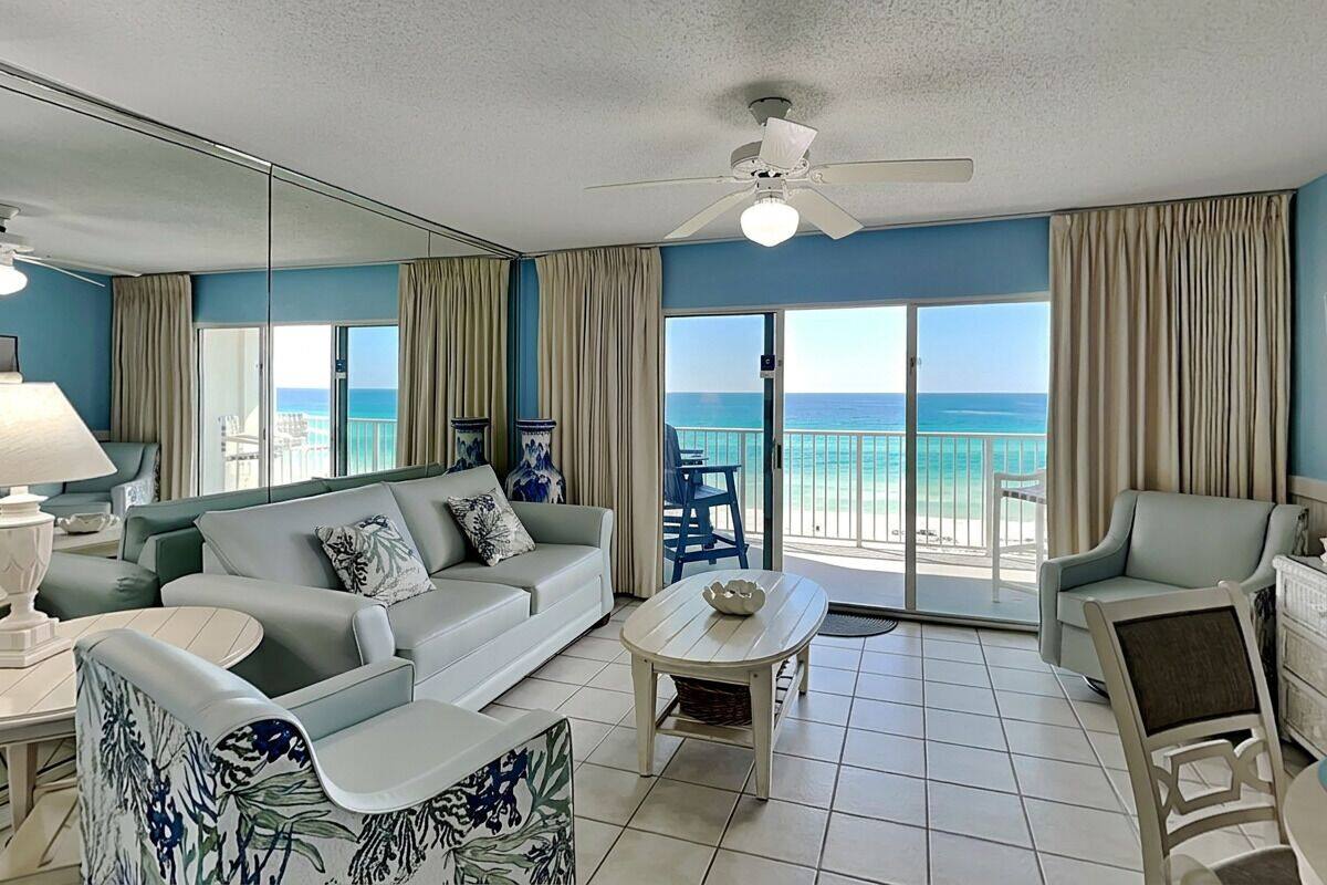 A living room with a sofa, armchair, coffee table, and a view of the ocean through large windows.