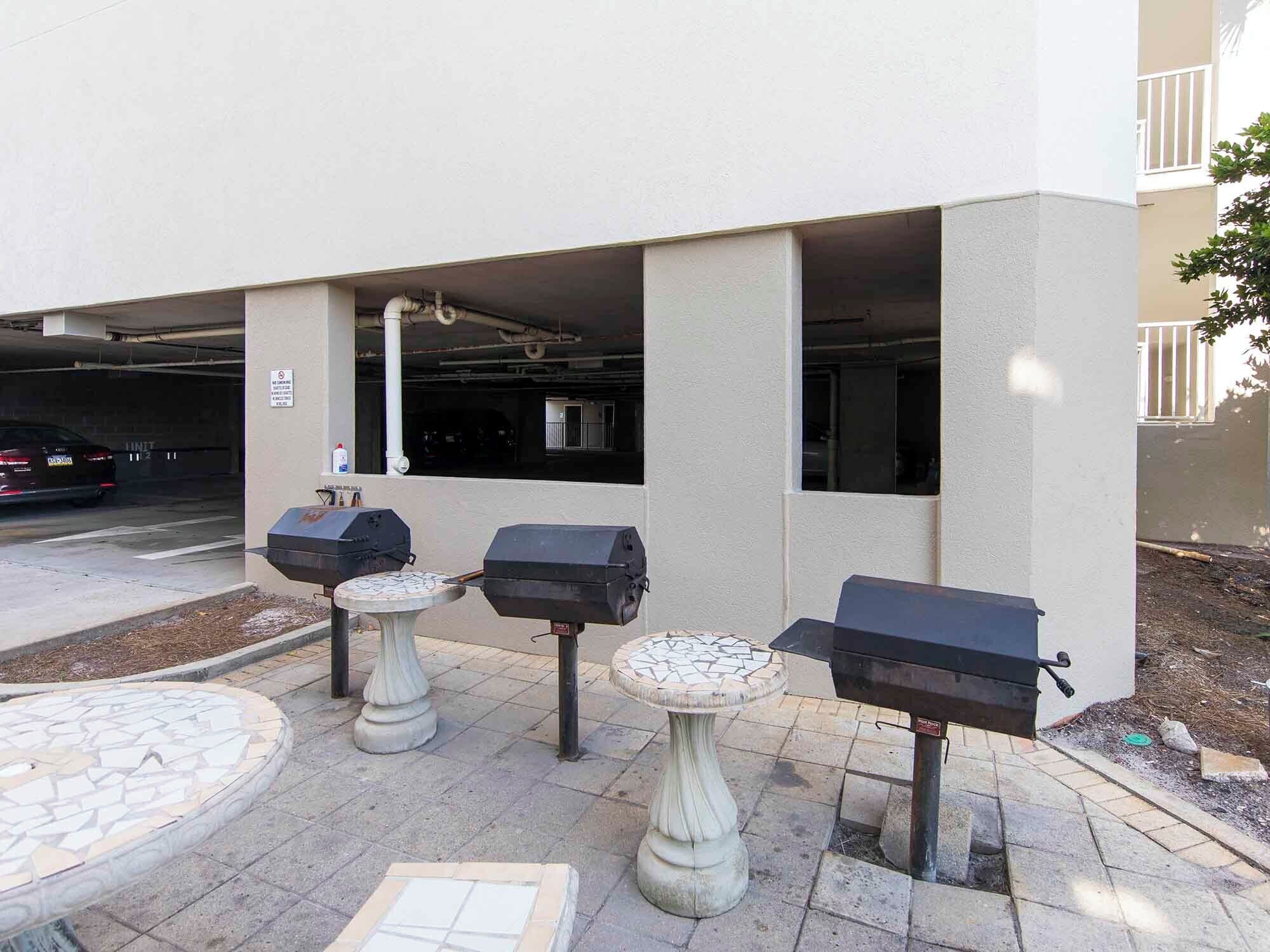 An outdoor patio area with three barbecue grills, a mosaic-tiled table, and a tiled floor.