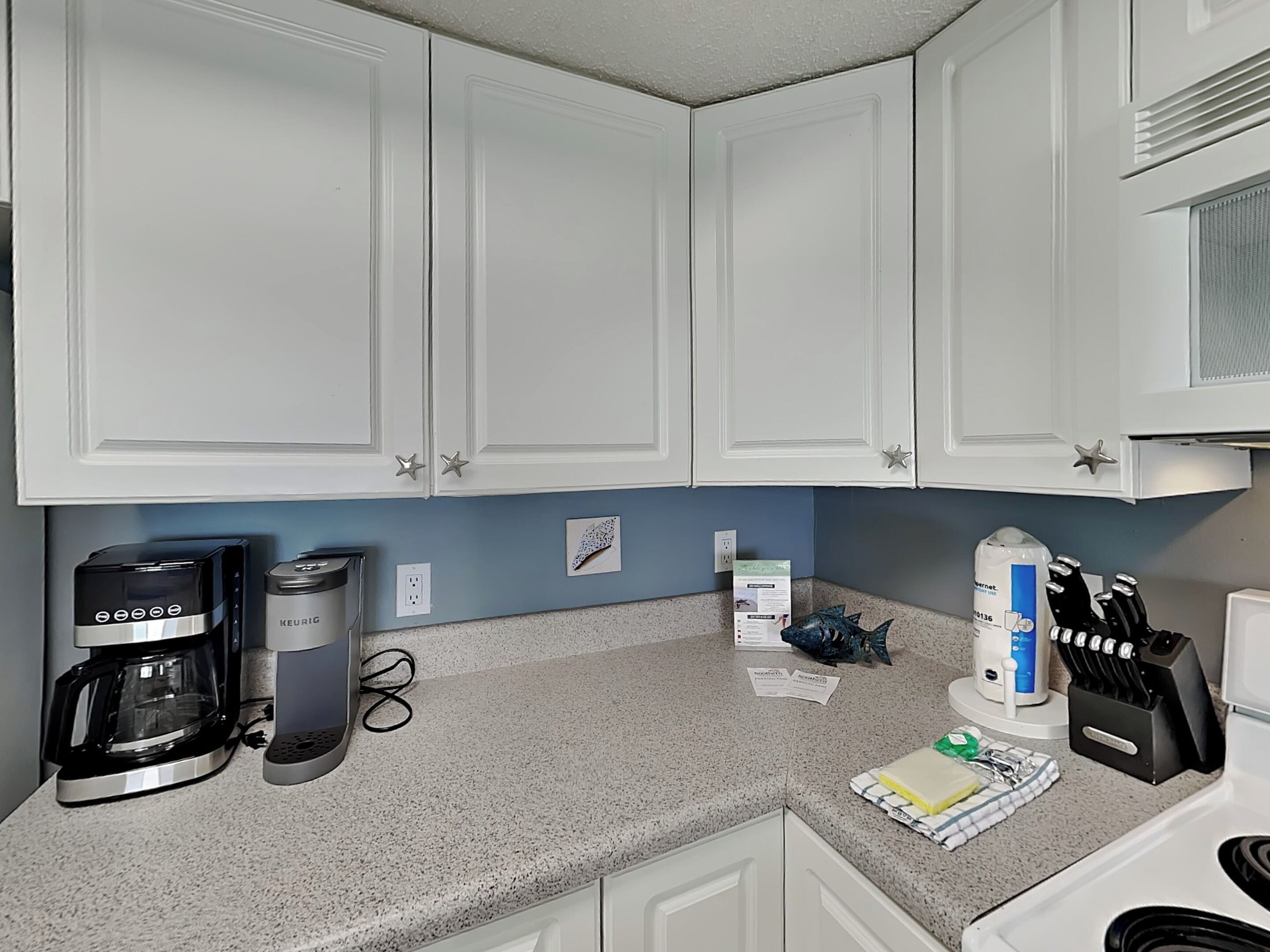 A kitchen with white cabinets, a coffee maker, a kettle, and a knife block.
