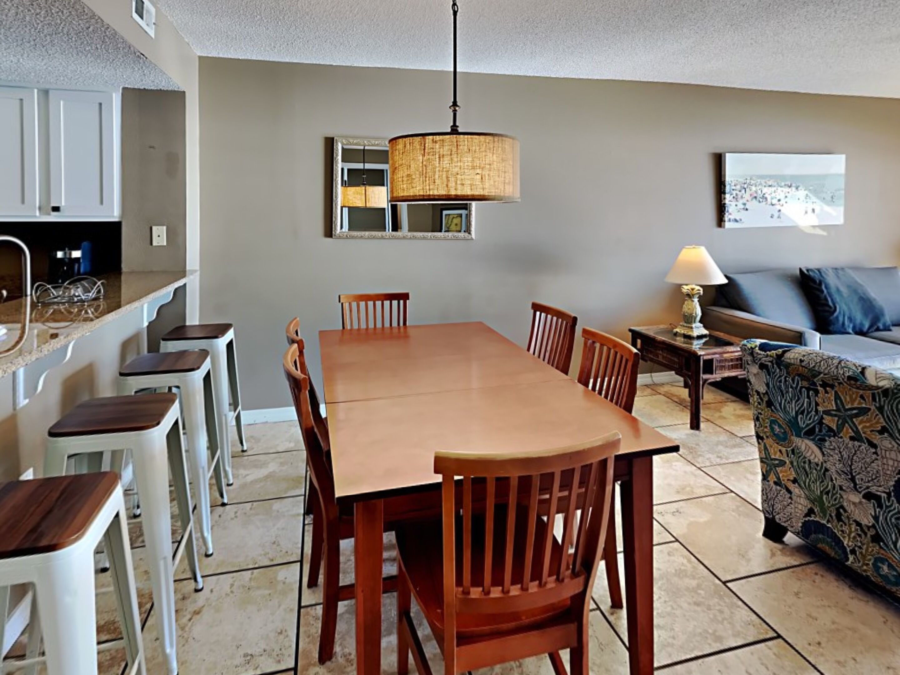 A dining area with a wooden table and chairs, a hanging light fixture, a sofa, and a patterned armchair.