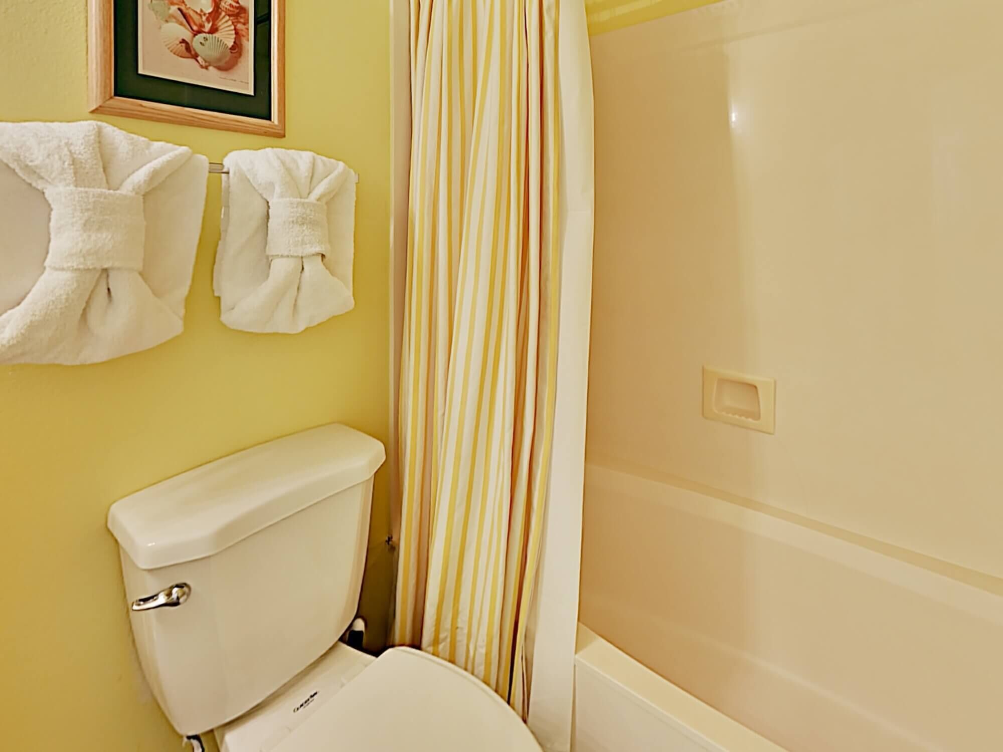 A bathroom with a toilet, a shower curtain, and two towels hanging on the wall.