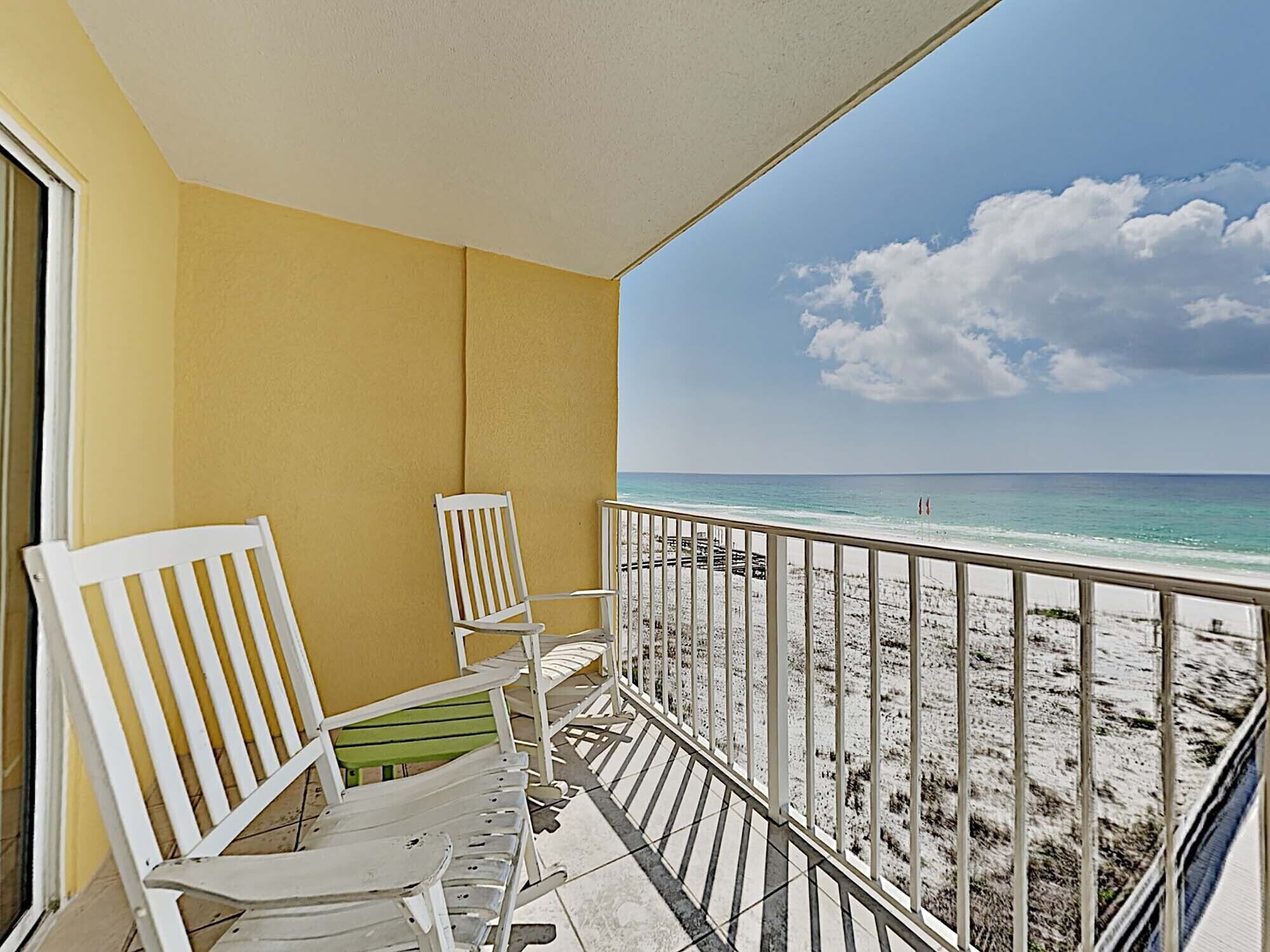 A balcony with white chairs and a view of the beach.
