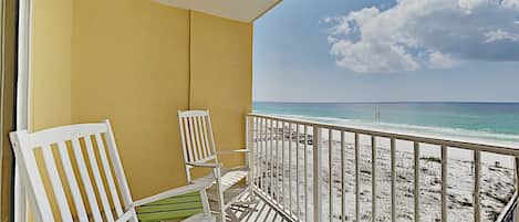 A balcony with white chairs and a view of the beach.