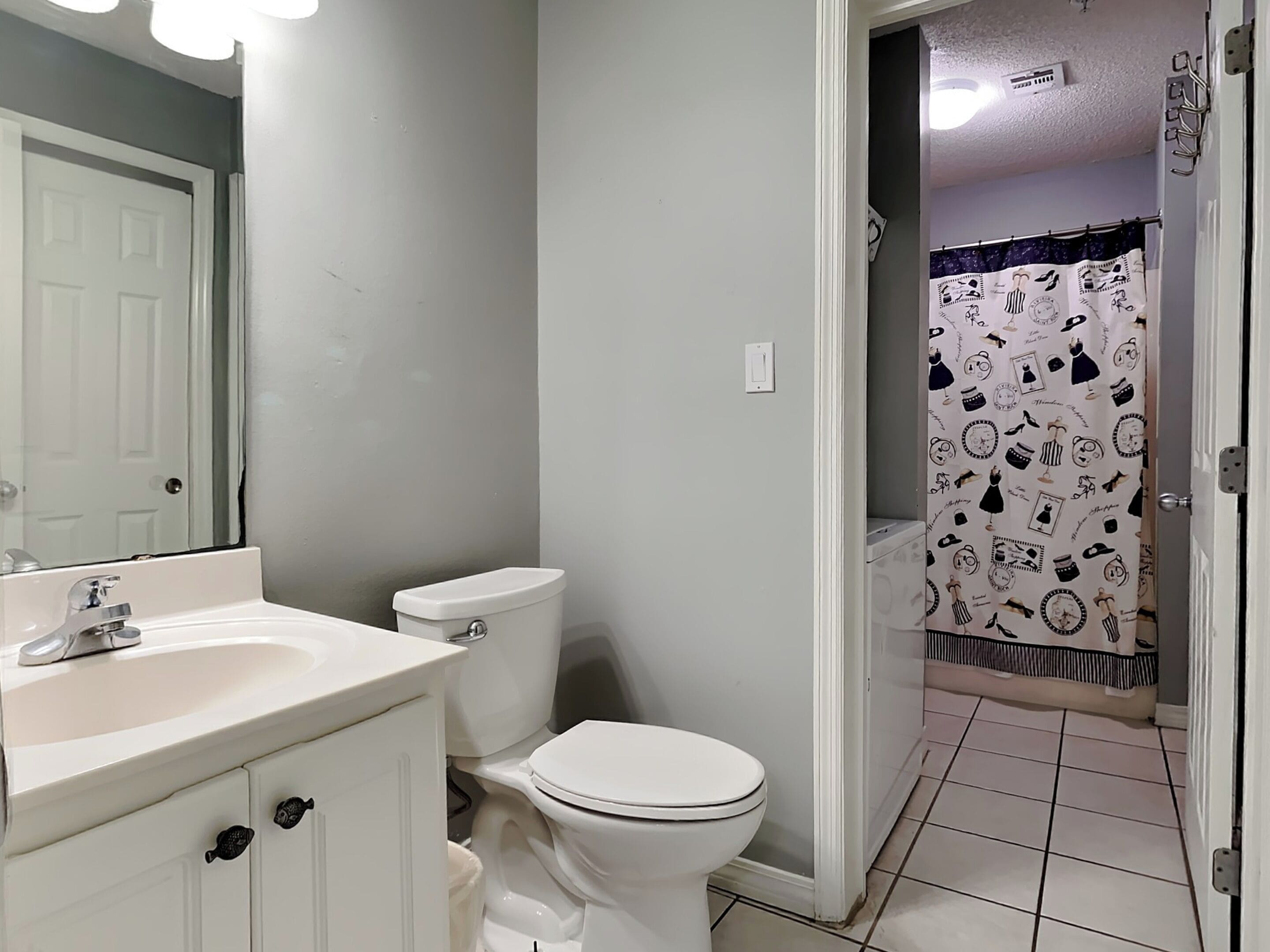 Un baño con lavamanos, inodoro y cortina de ducha estampada.