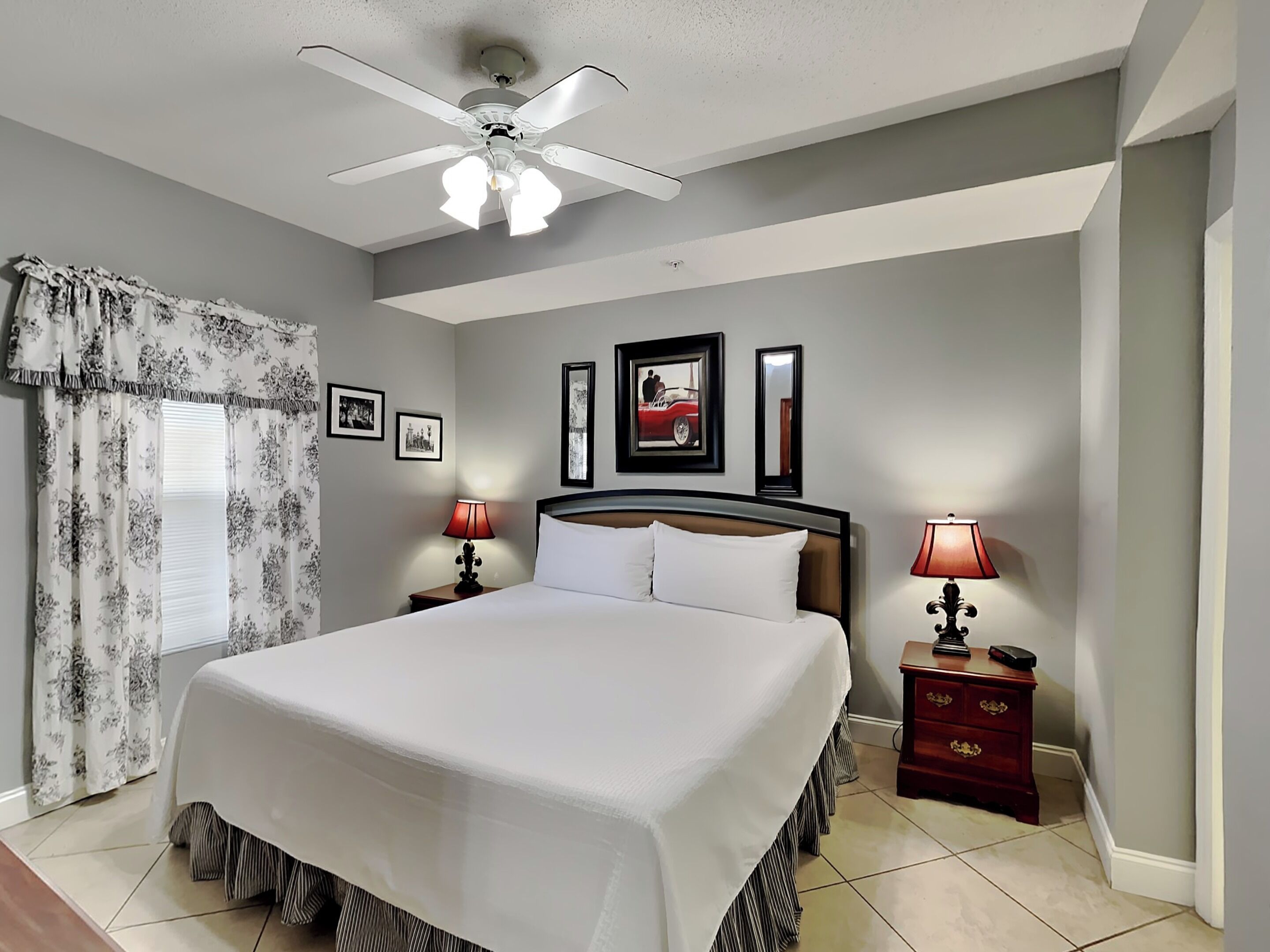 A bedroom with a large bed, two bedside tables with lamps, a ceiling fan, and framed pictures on the wall.