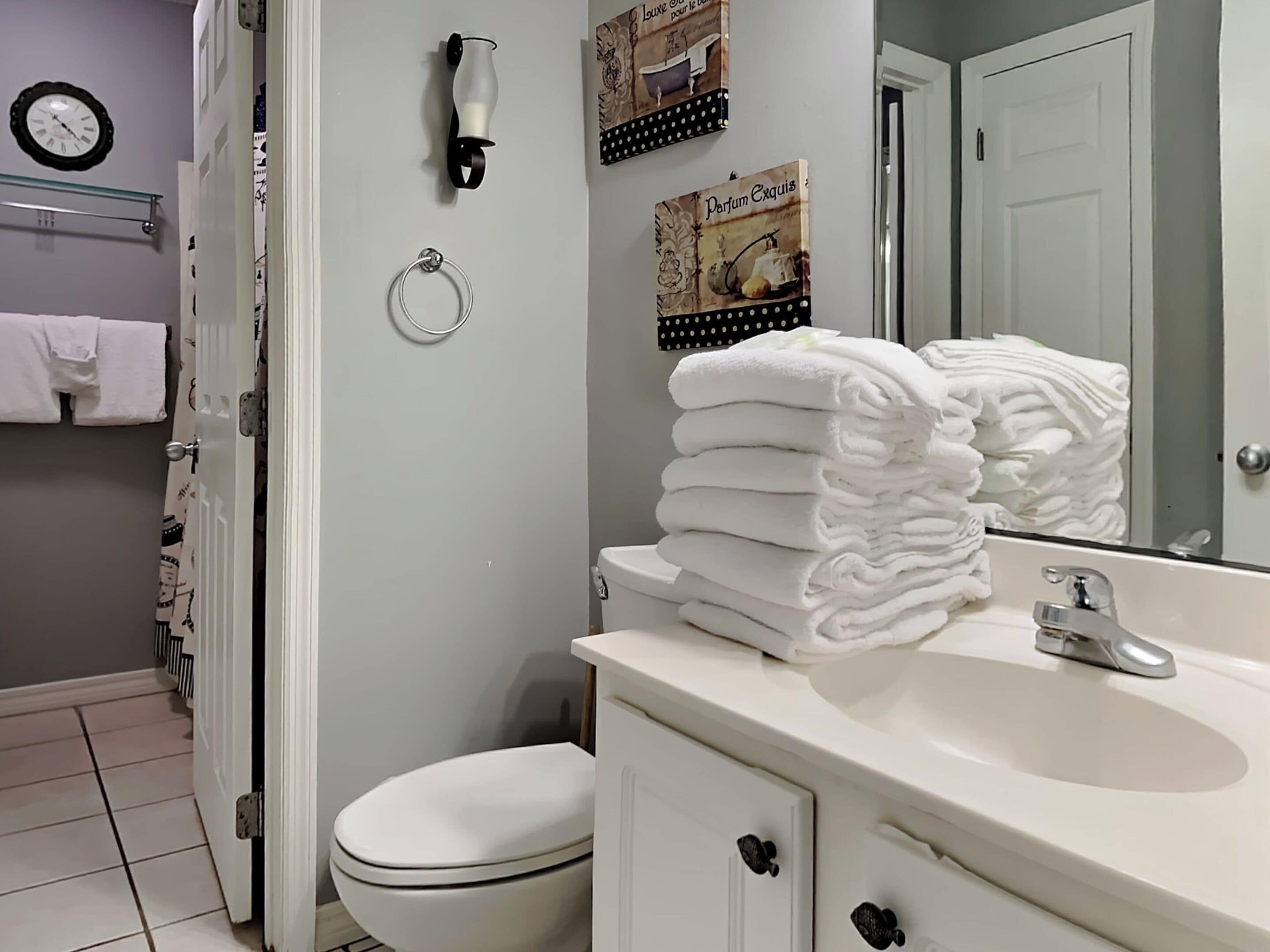 A bathroom with a toilet, sink, and a stack of white towels.