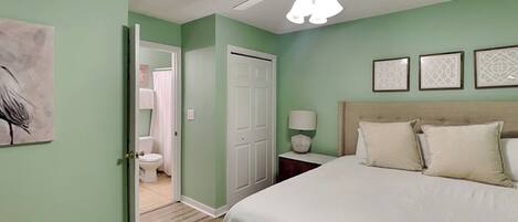 A bedroom with a bed, a nightstand, a ceiling fan, and a door leading to a bathroom.