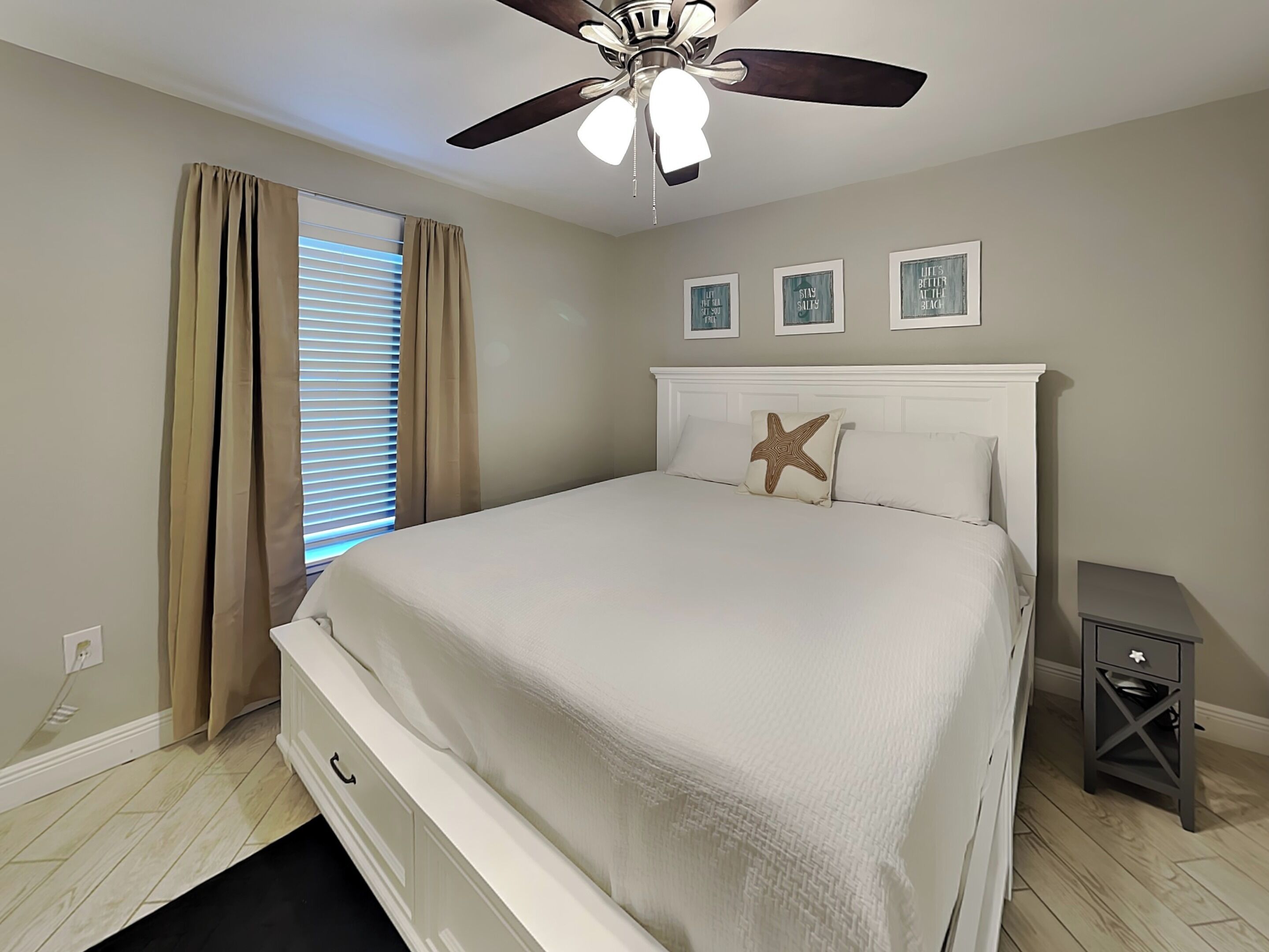A bedroom with a bed, a ceiling fan, a nightstand, and a window with curtains.
