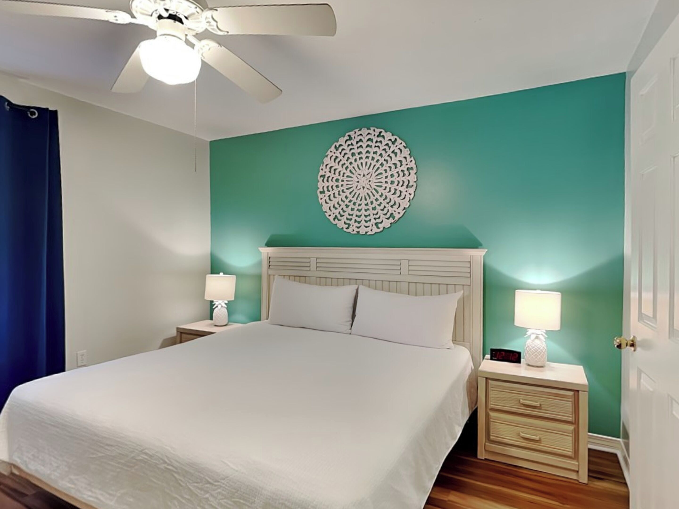 Une chambre à coucher bien rangée, avec un lit, deux tables de chevet, un ventilateur de plafond et un élément décoratif mural.