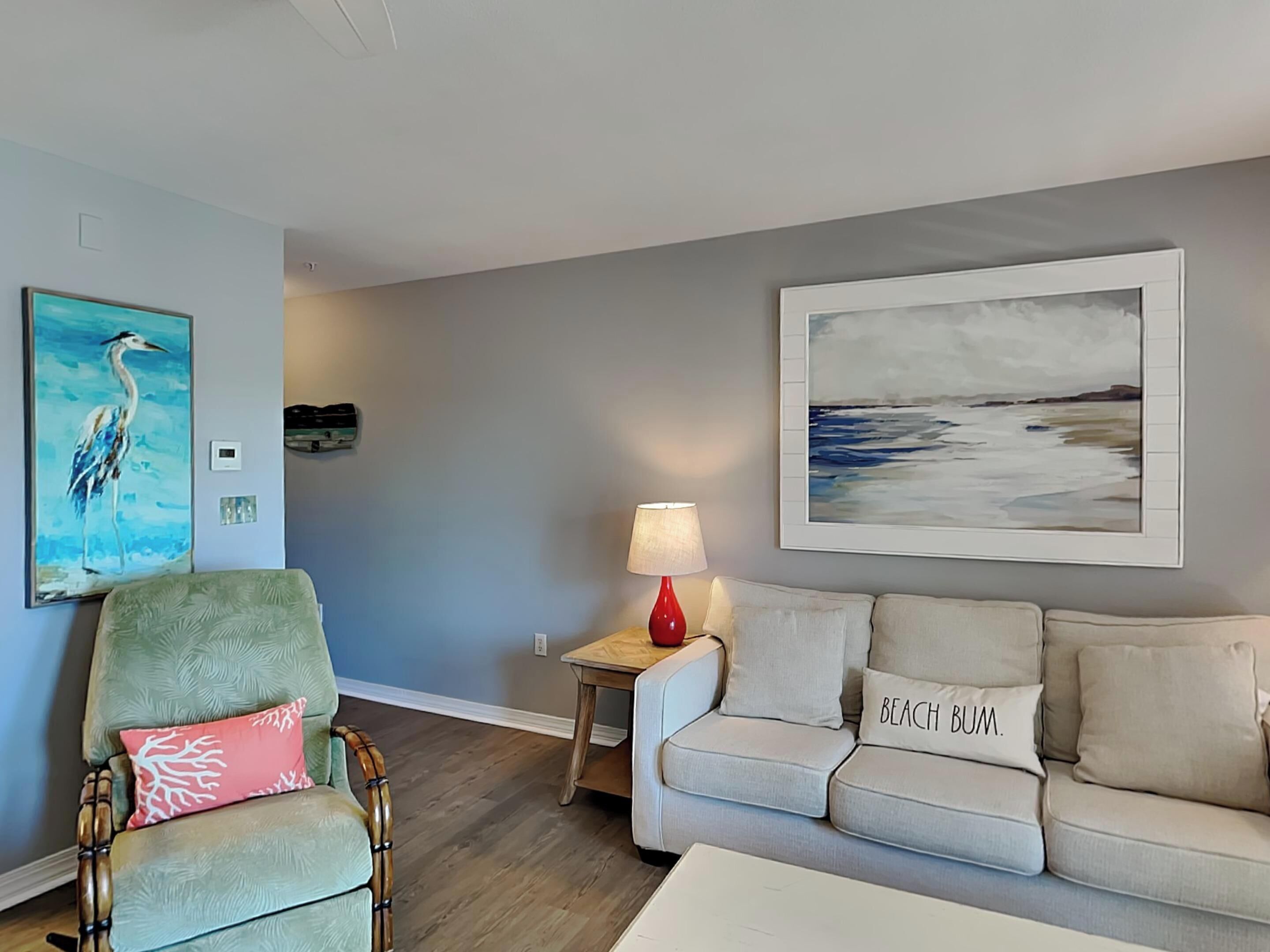 Una sala de estar con un sillón verde, un sofá color beige, una lámpara roja y dos cuadros en la pared.