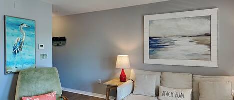 Una sala de estar con un sillón verde, un sofá color beige, una lámpara roja y dos cuadros en la pared.