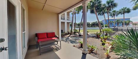 A covered outdoor area with a red sofa, a metal table, and a view of palm trees and a building in the background.