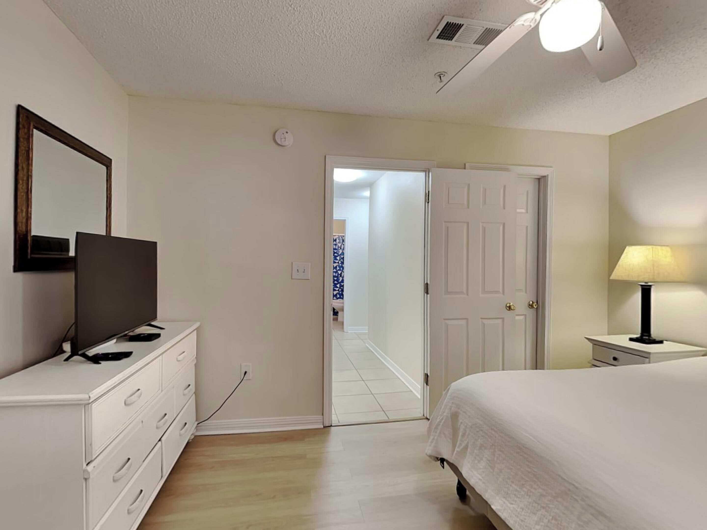Une chambre à coucher avec un lit, un téléviseur posé sur une commode, une lampe et une porte donnant sur une autre pièce.
