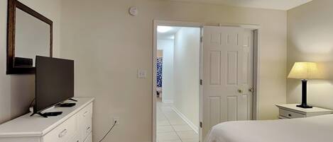 Une chambre à coucher avec un lit, un téléviseur posé sur une commode, une lampe et une porte donnant sur une autre pièce.
