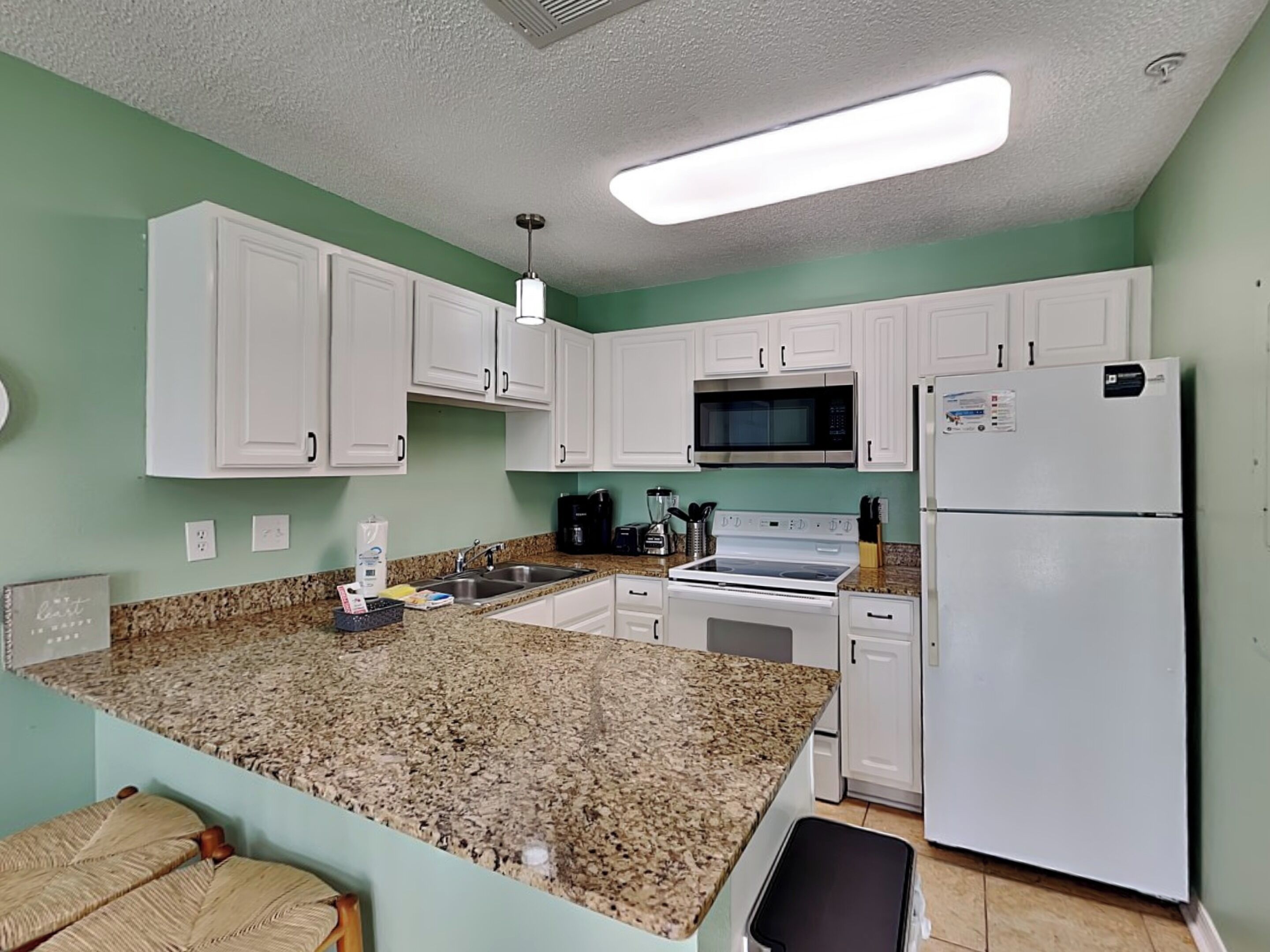 Una cocina con armarios blancos, encimera de granito, microondas, estufa y refrigerador.