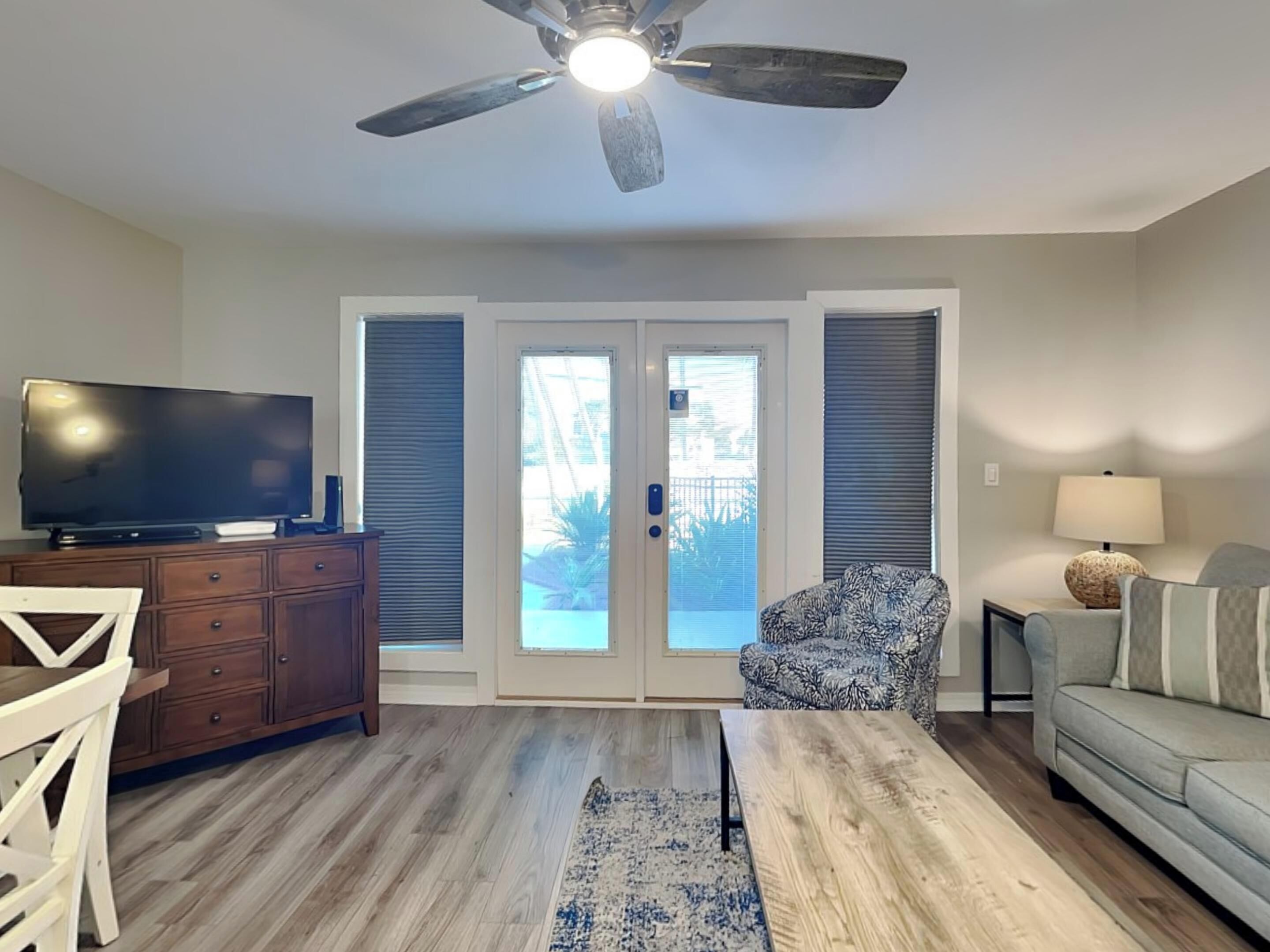 A living room with a ceiling fan, a television on a wooden cabinet, a patterned armchair, a sofa, and a coffee table.
