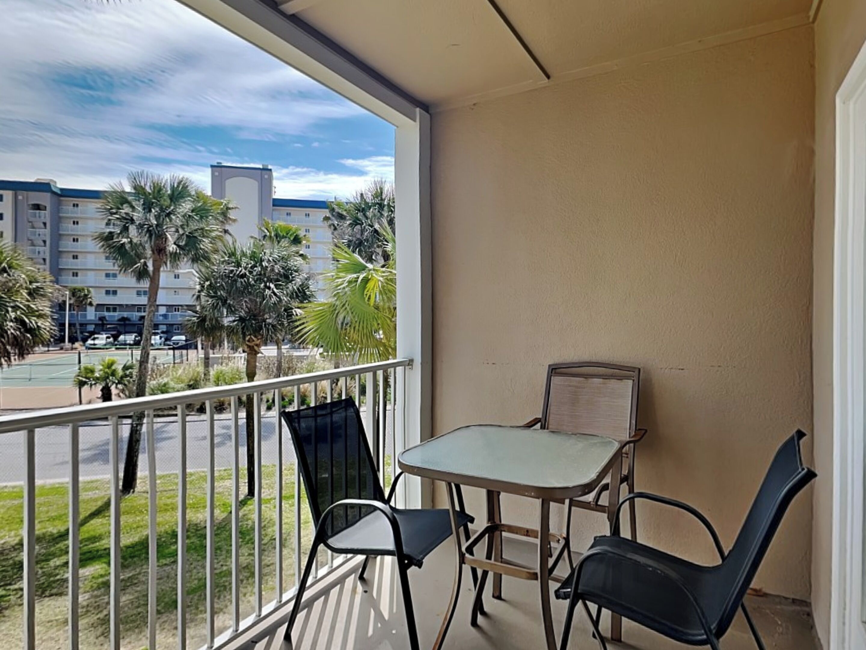 Ein Balkon mit Tisch und zwei Stühlen, mit Blick auf einen Parkplatz und Gebäude.