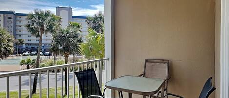 A balcony with a table and two chairs, overlooking a parking lot and buildings.