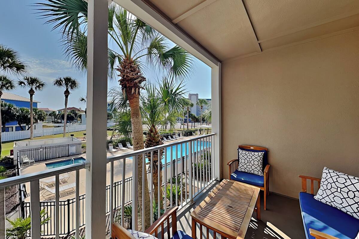 Ein Balkon mit Blick auf einen Pool, Holzmöbel und Palmen.