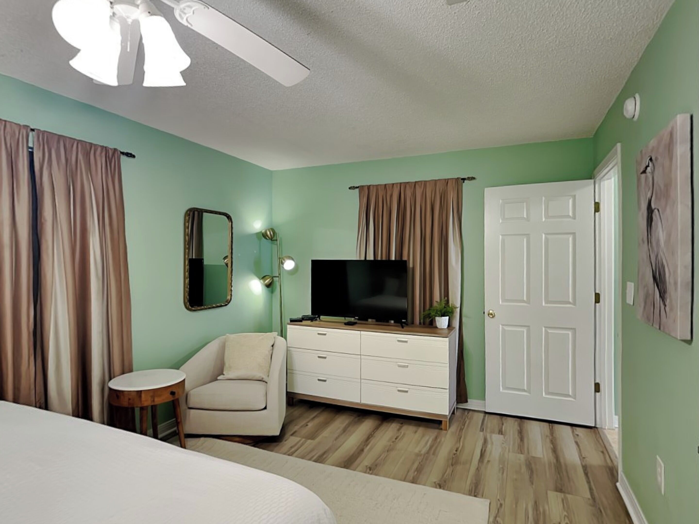 A bedroom with a bed, a chair, a dresser, a television, and a door.