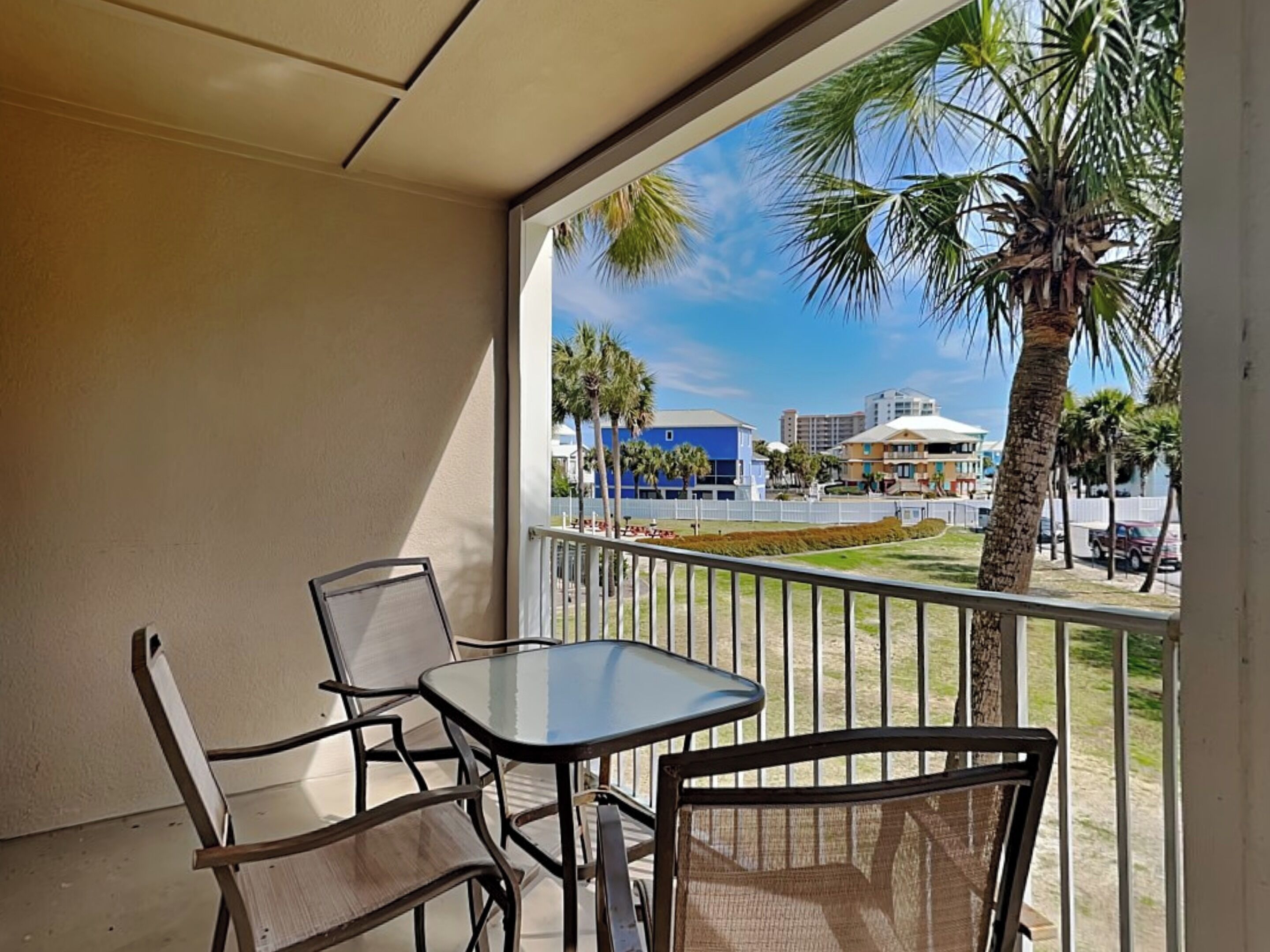 A balcony with a table and chairs, overlooking a residential area with palm trees and buildings.