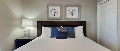 Un lit bien fait, avec une literie blanche et des oreillers bleus, une lampe de chevet et deux œuvres d’art encadrées accrochées au mur au-dessus.