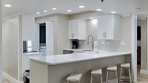 Une cuisine moderne avec des meubles blancs, un îlot central doté de tabourets et un éclairage encastré au plafond.