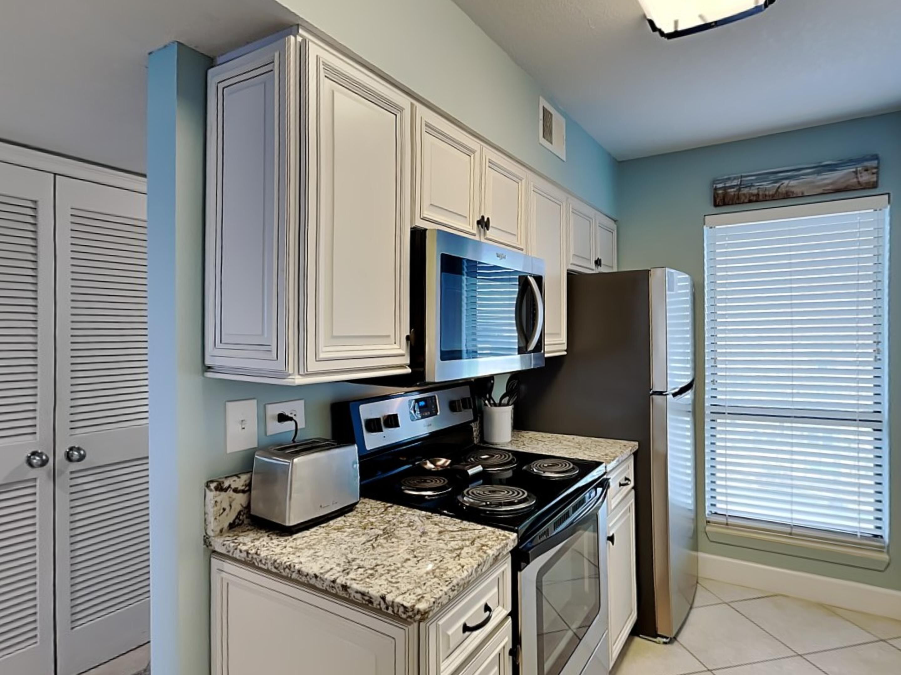 A kitchen with white cabinets, a microwave, a stove, a toaster, and a refrigerator.