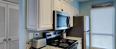 A kitchen with white cabinets, a microwave, a stove, a toaster, and a refrigerator.