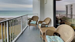 Un balcon doté de meubles en osier et offrant une vue sur la plage et l’océan.