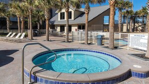 Une piscine dont le bord est revêtu de carrelage, entourée de chaises longues et de palmiers, avec un bâtiment visible au loin.