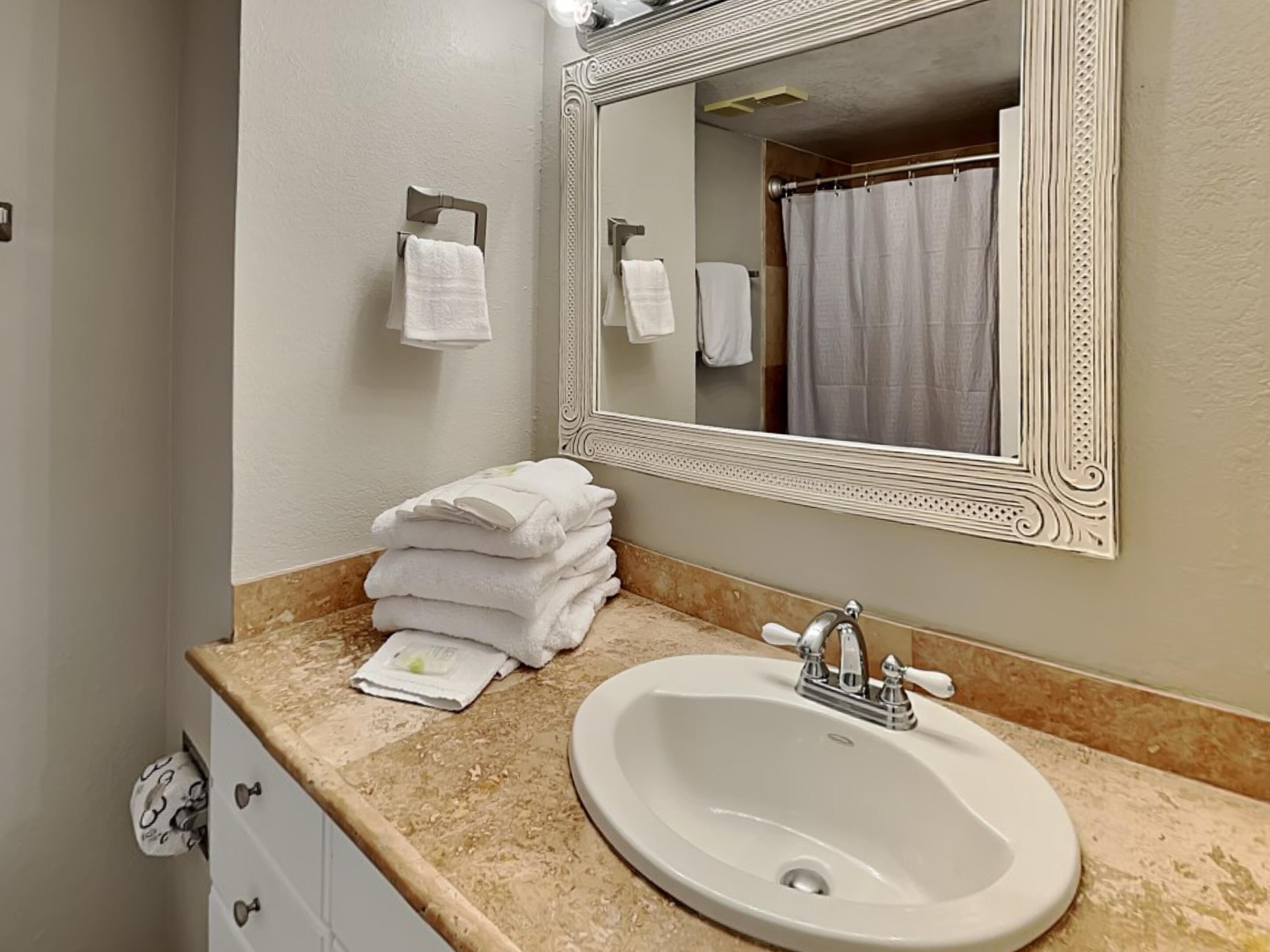 A bathroom with a sink, mirror, and stacked towels.