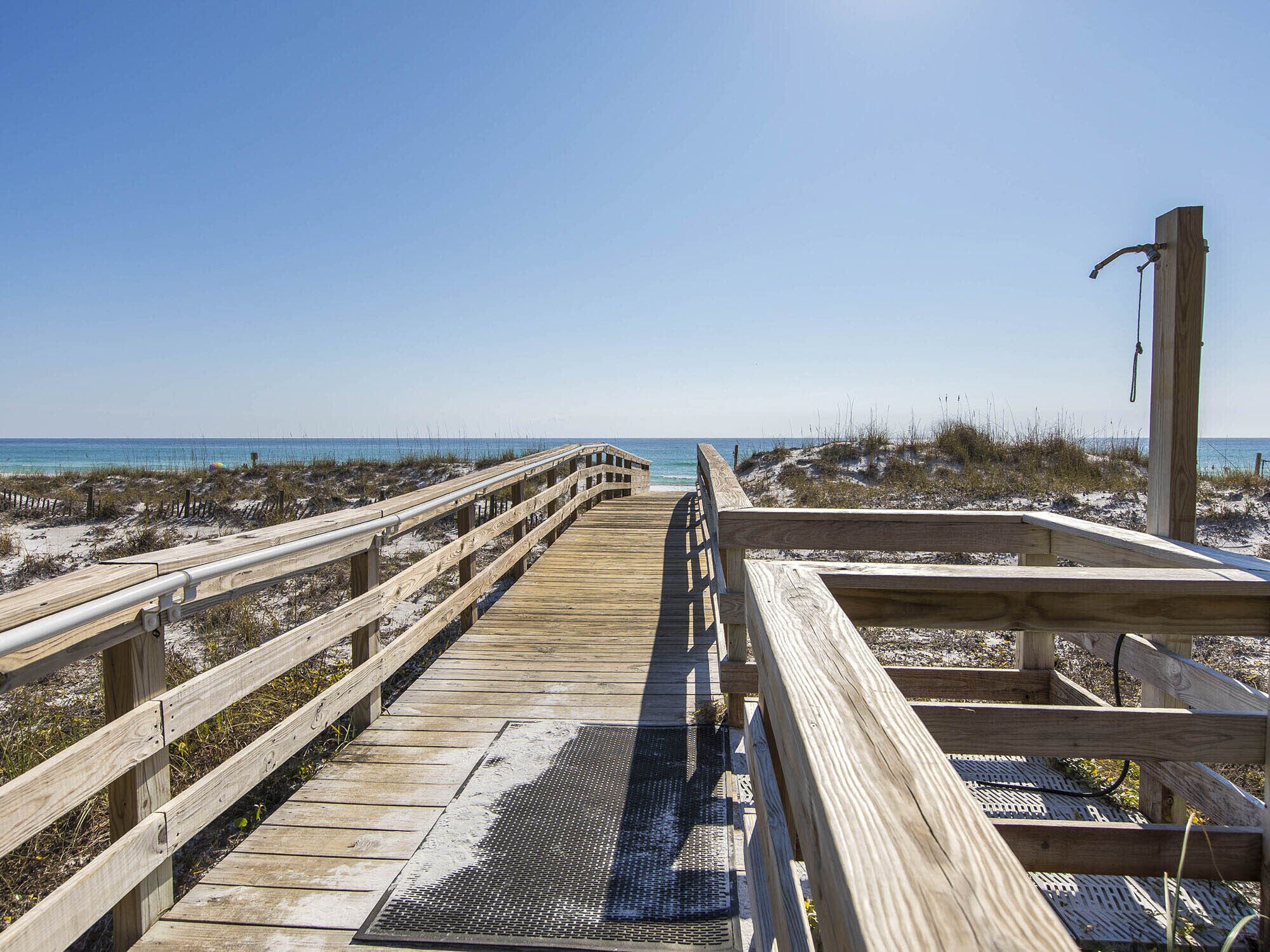 A wooden boardwalk leading to the beach with a metal grate at the end.