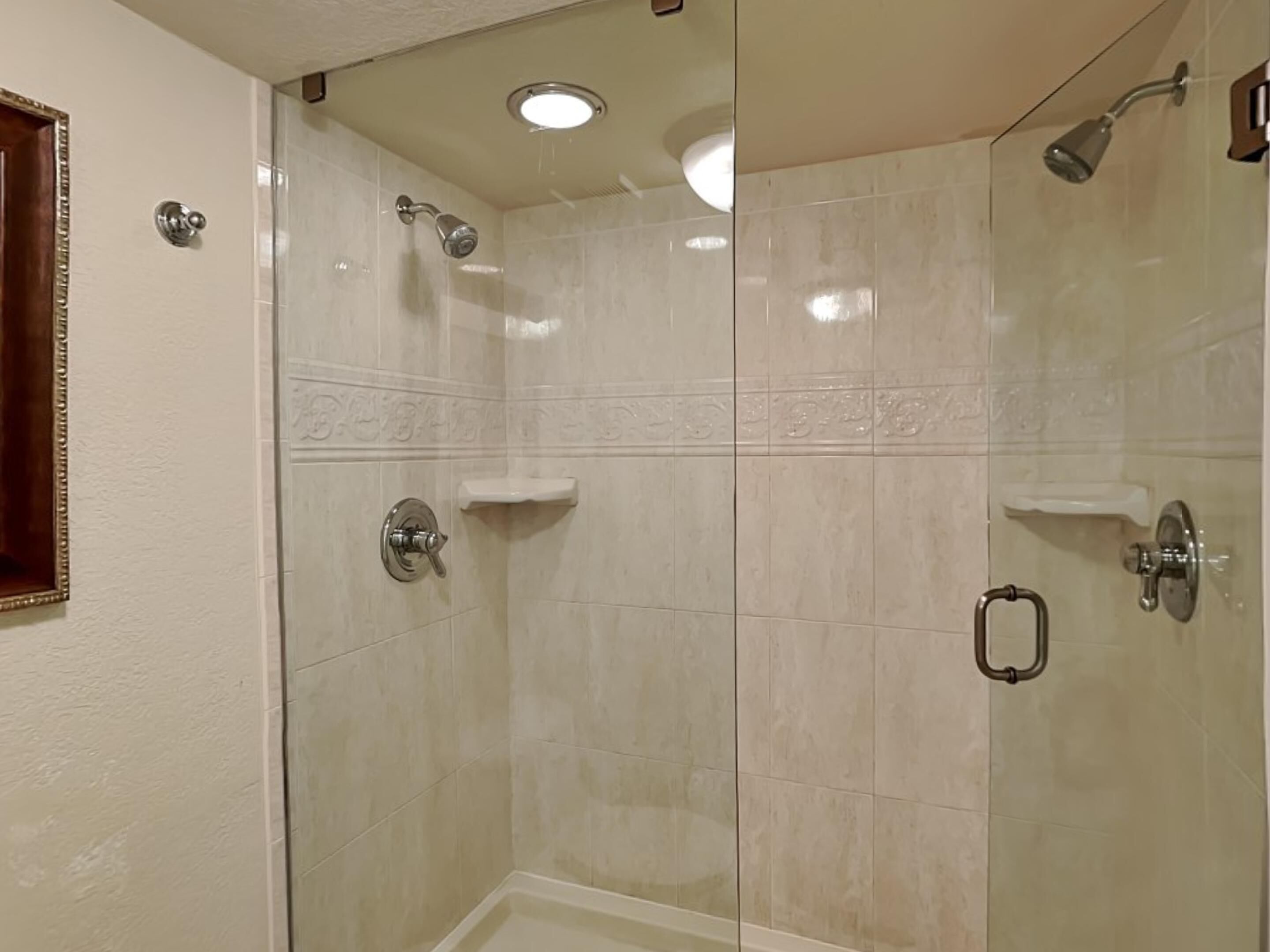 A glass-enclosed shower with a handheld showerhead, a wall-mounted faucet, and a small shelf.