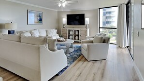 Un salon moderne avec un grand canapé, une table basse, un téléviseur et un ventilateur de plafond.