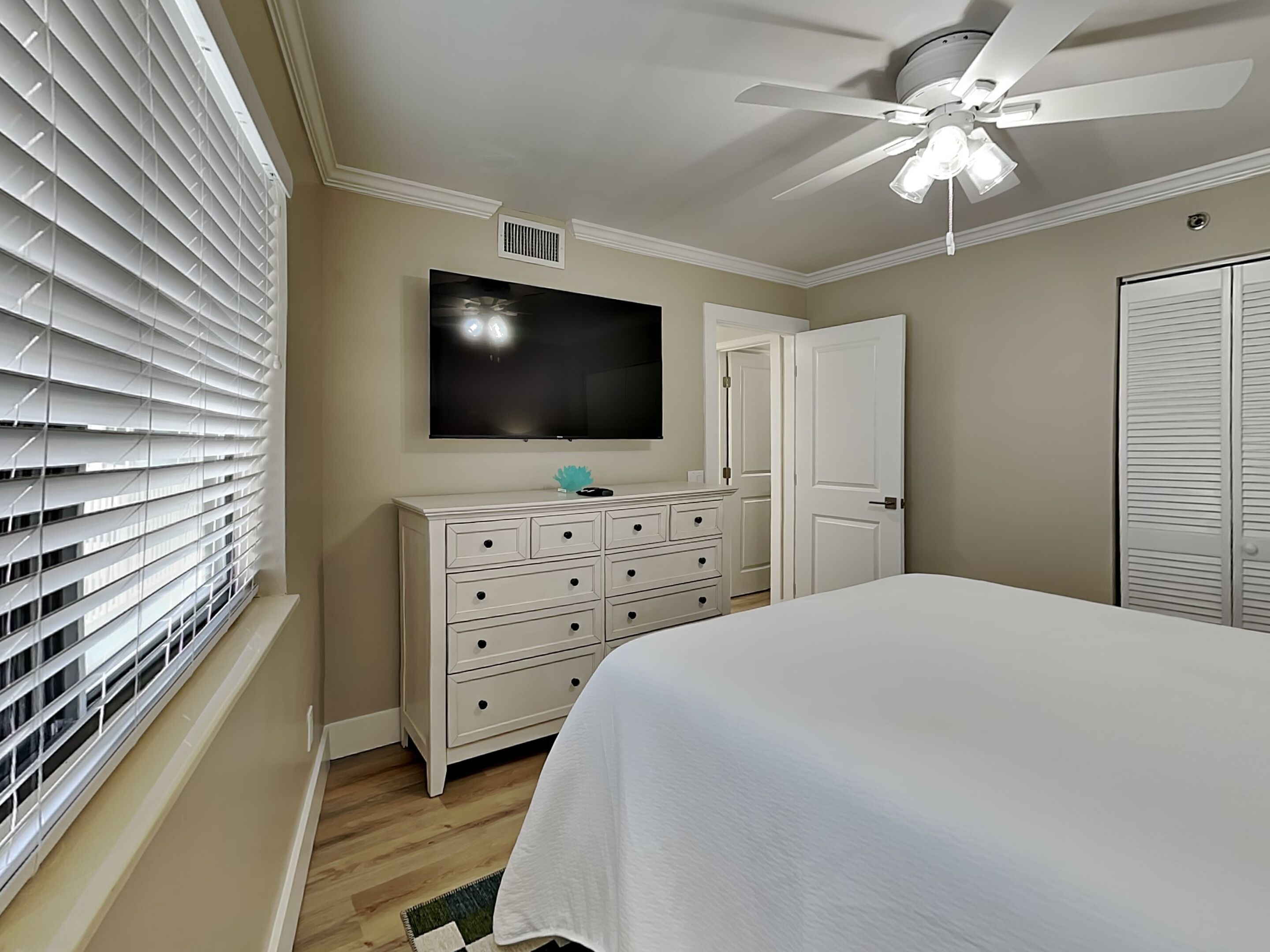 Ein Schlafzimmer mit Bett, Kommode, Fernseher und Deckenventilator.
