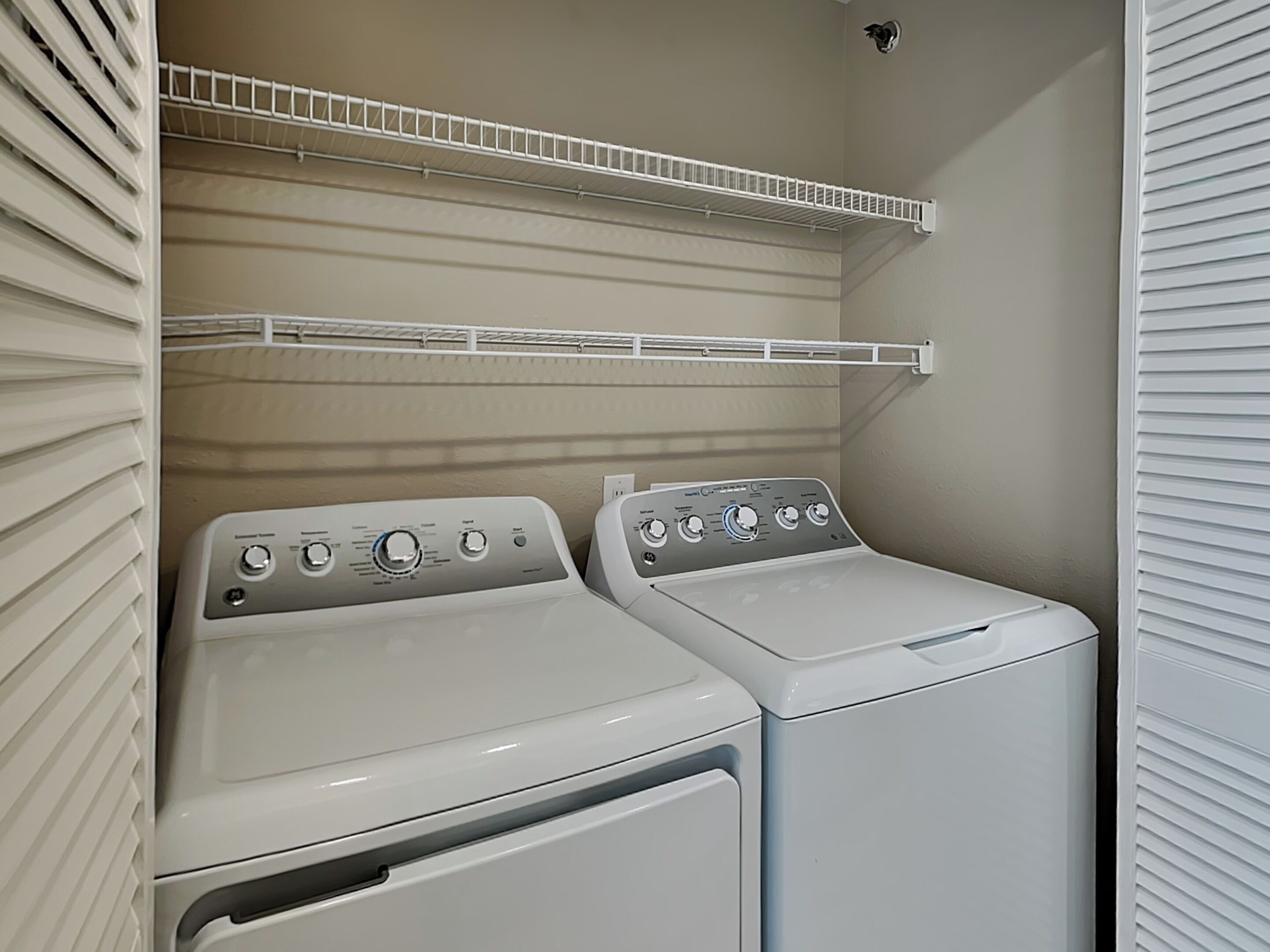 A laundry area with two white front-loading washing machines and a metal shelf above them.