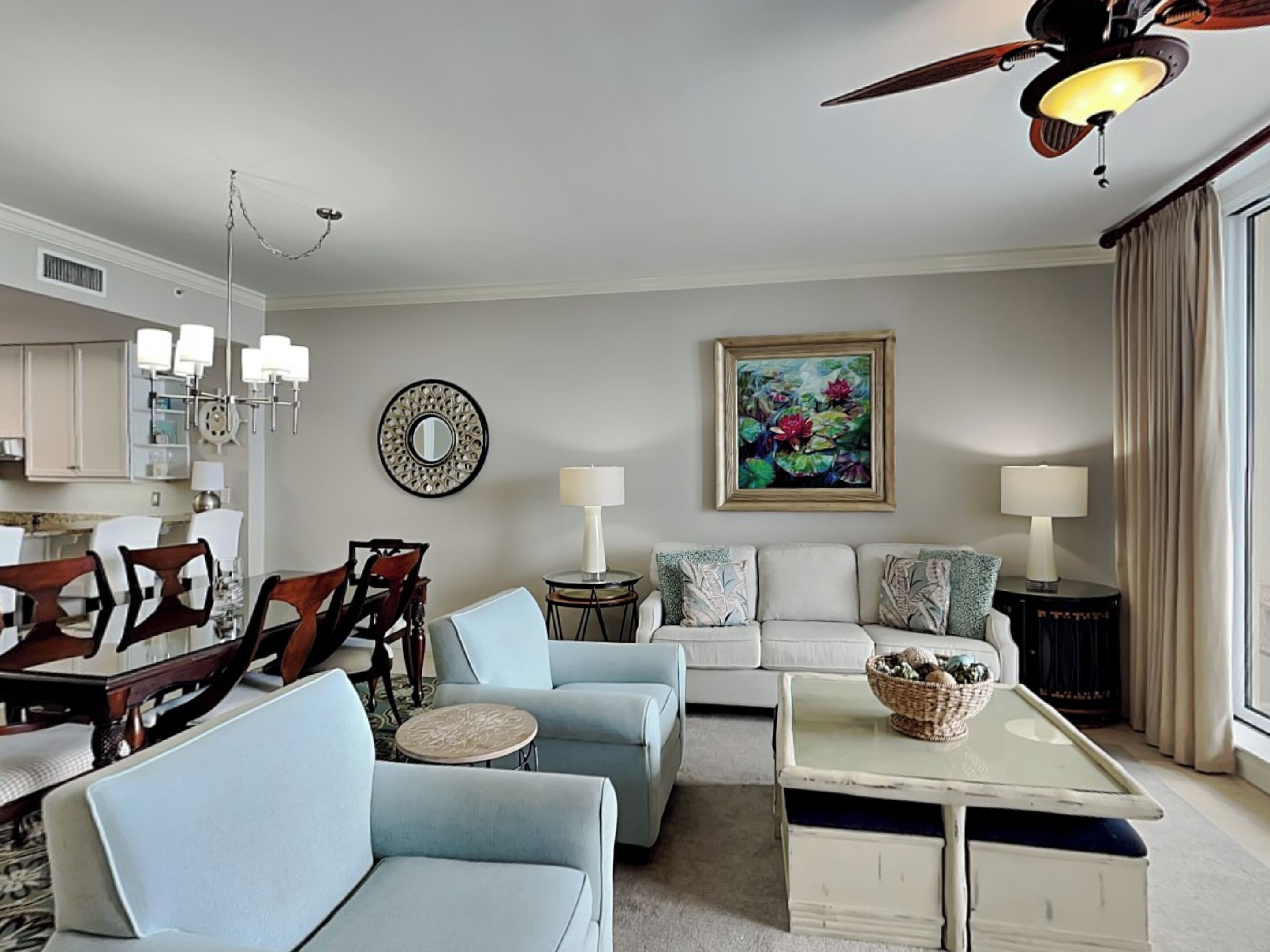 A living room with a dining area, a ceiling fan, a painting, and a lamp.