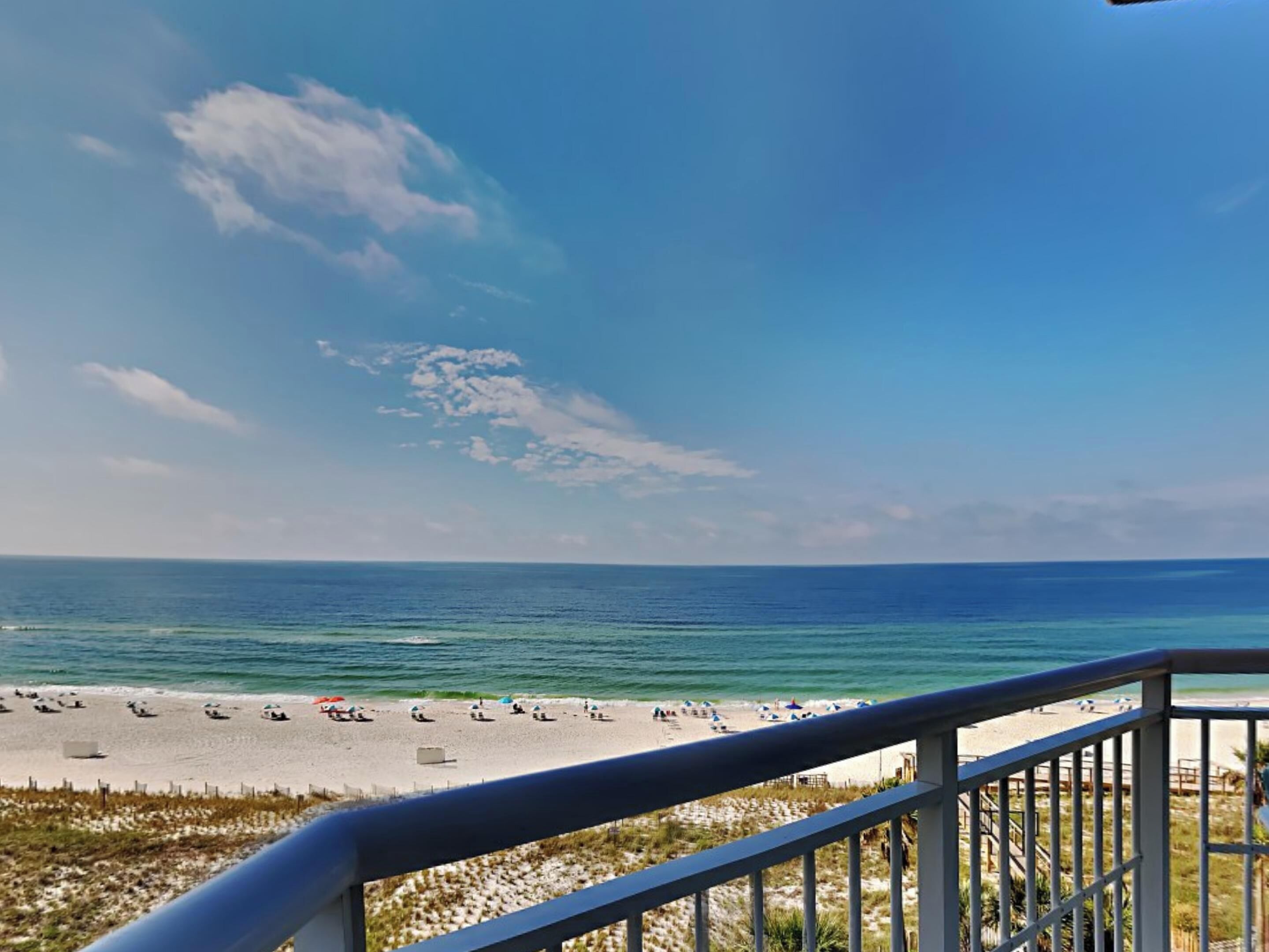 A beach view from a balcony with a railing, sandy beach, and ocean.