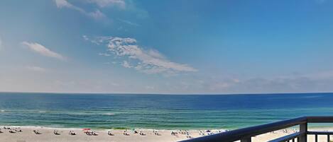 A beach view from a balcony with a railing, sandy beach, and ocean.